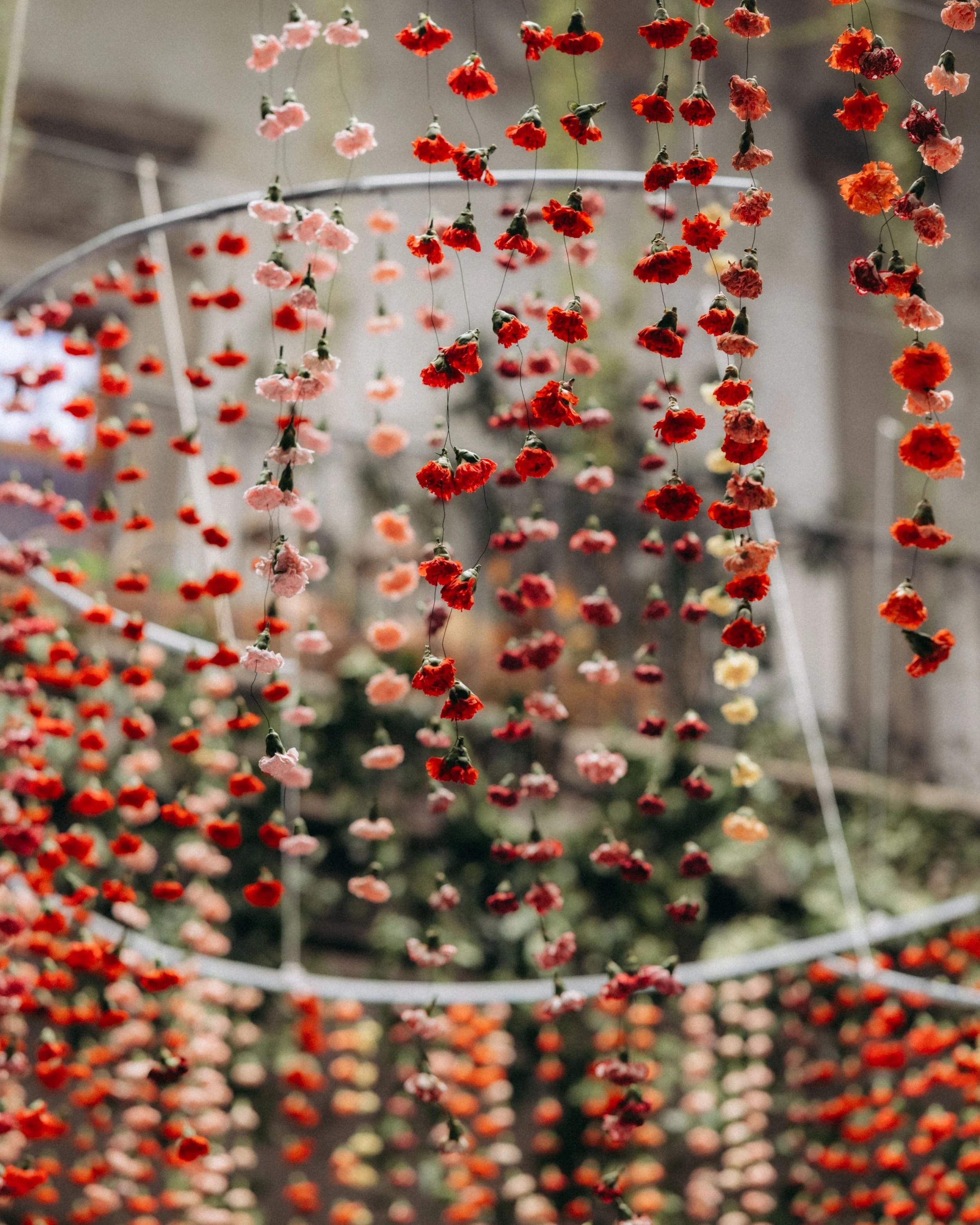 Hanging strings of pink, red, orange, and yellow flowers in an outdoor setting.