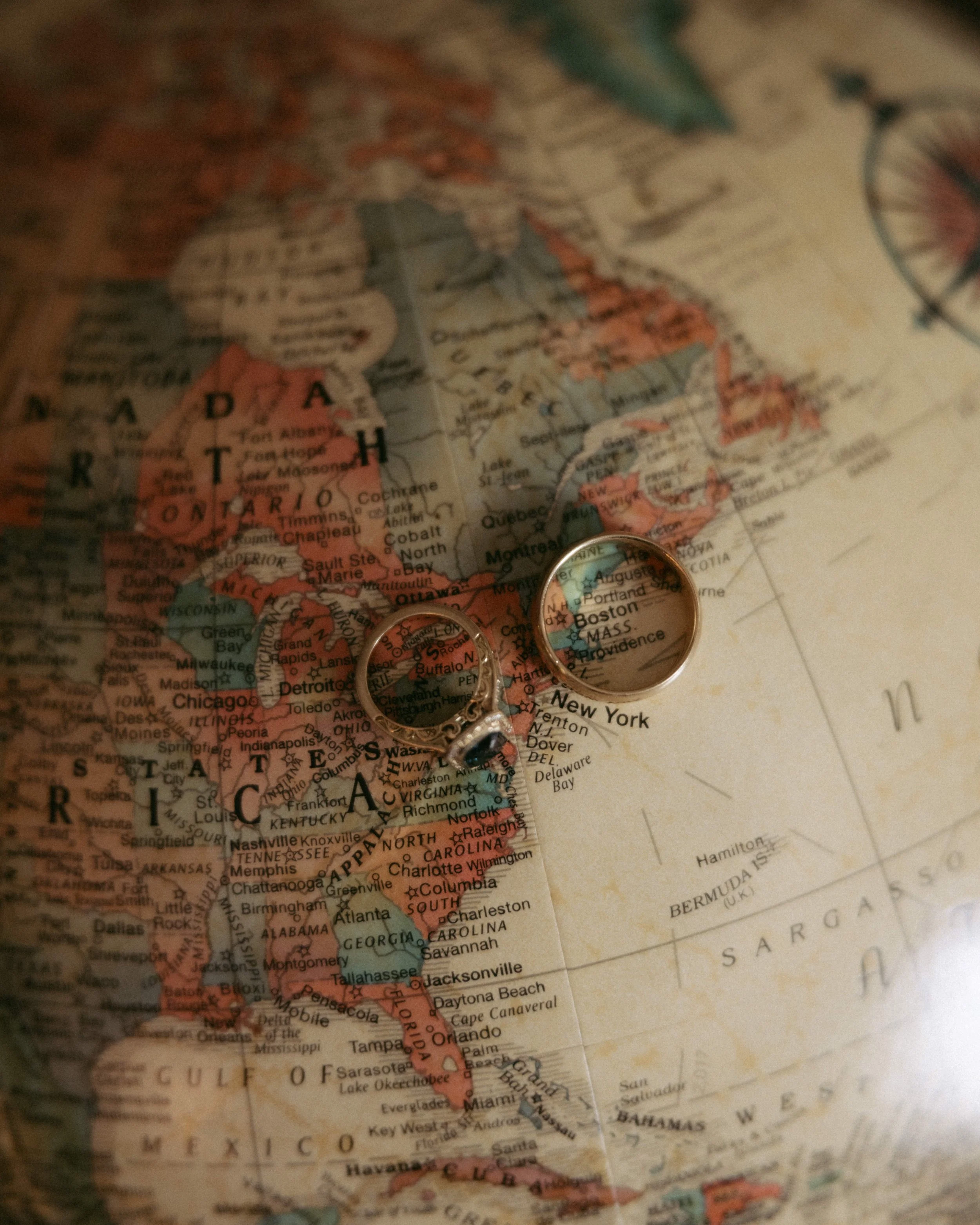 Close-up of a vintage map of North America, showing the United States, Canada, and surrounding countries with two wedding rings placed on the map.