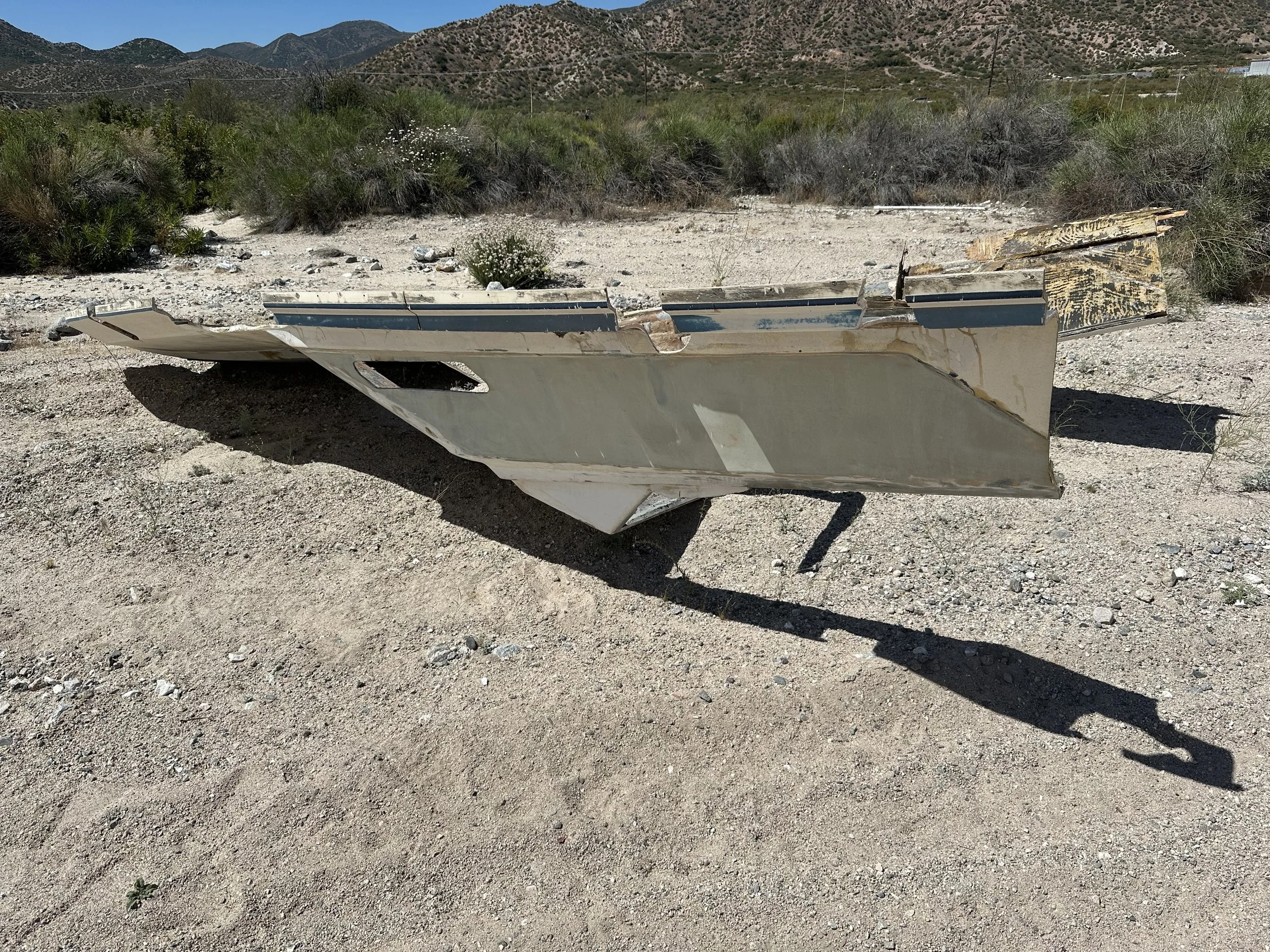 A discarded boat in the dirt with mountains in the background.