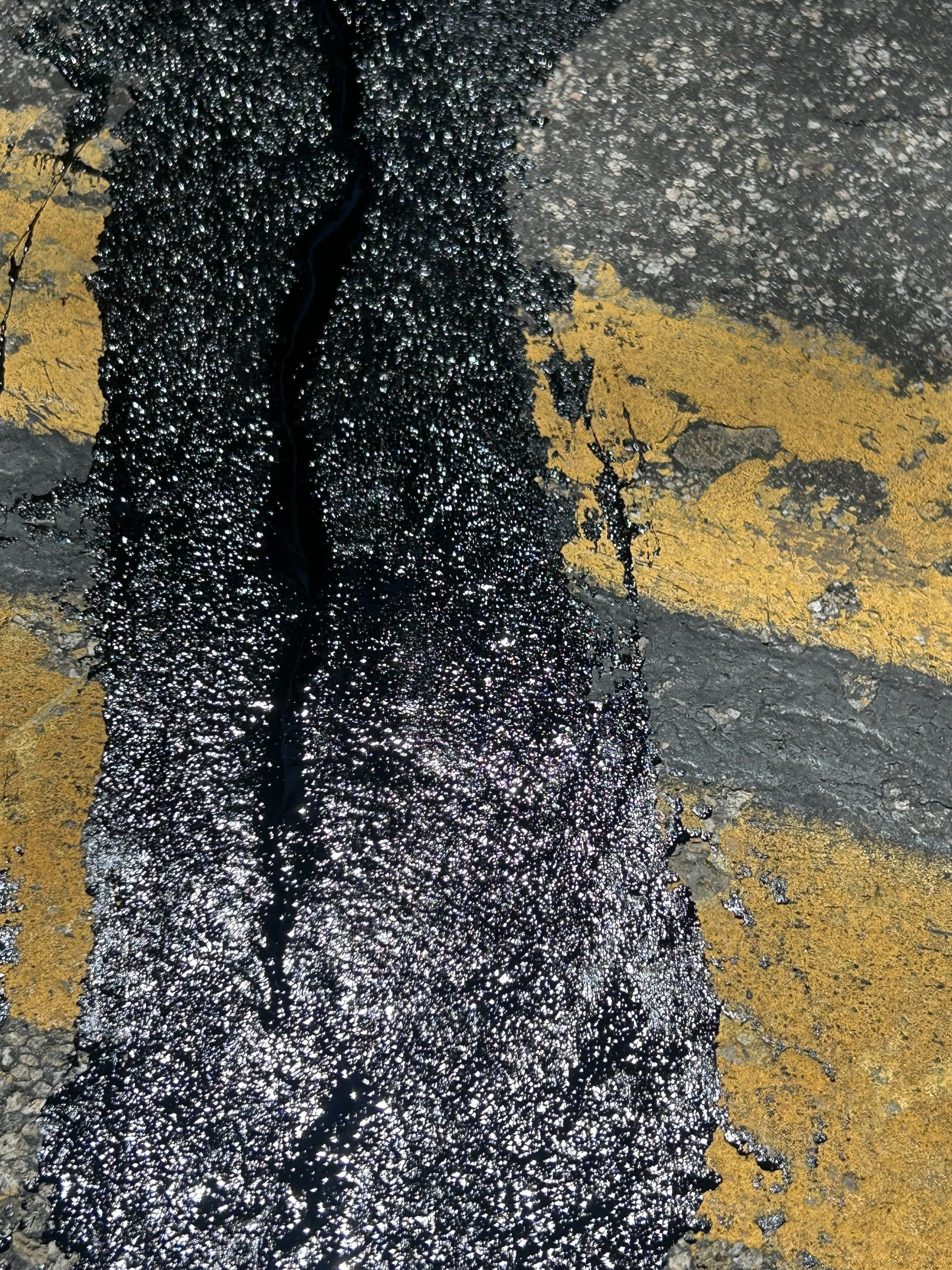 Fresh asphalt crack repair laid across the yellow lines of a street.