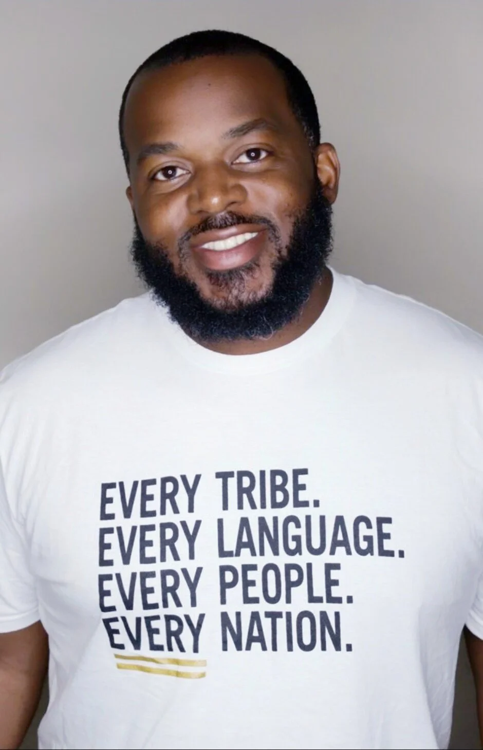 Man smiling, wearing a t-shirt with the text "Every Tribe. Every Language. Every People. Every Nation."