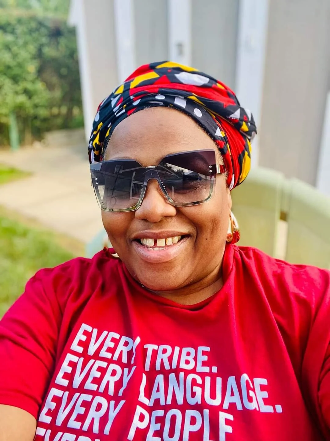 Smiling person wearing sunglasses, colorful headscarf, and a red t-shirt with white text that says "Every tribe. Every language. Every people."