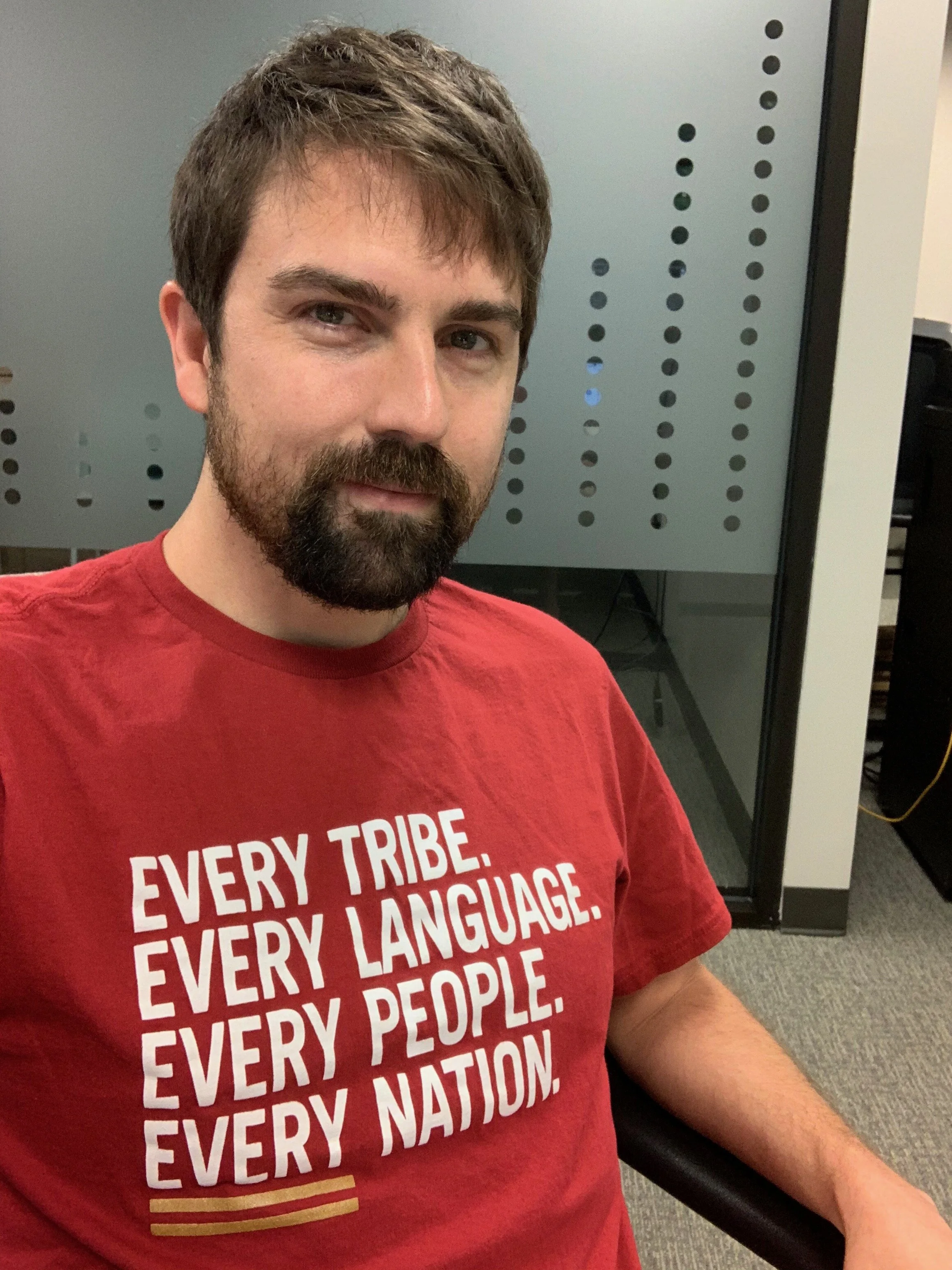 Man with beard wearing a red t-shirt with text "EVERY TRIBE. EVERY LANGUAGE. EVERY PEOPLE. EVERY NATION."