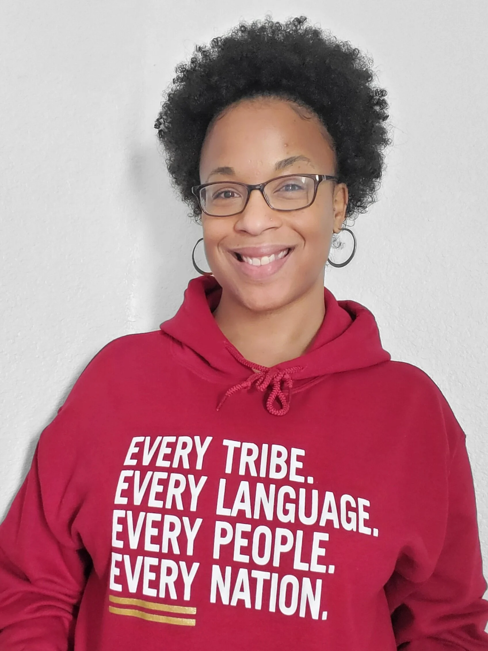 Person wearing glasses and a red hoodie with text "Every tribe. Every language. Every people. Every nation." smiling.
