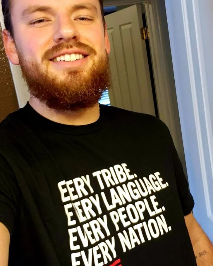 Man with a beard wearing a black t-shirt with white text "EVERY TRIBE. EVERY LANGUAGE. EVERY PEOPLE. EVERY NATION."