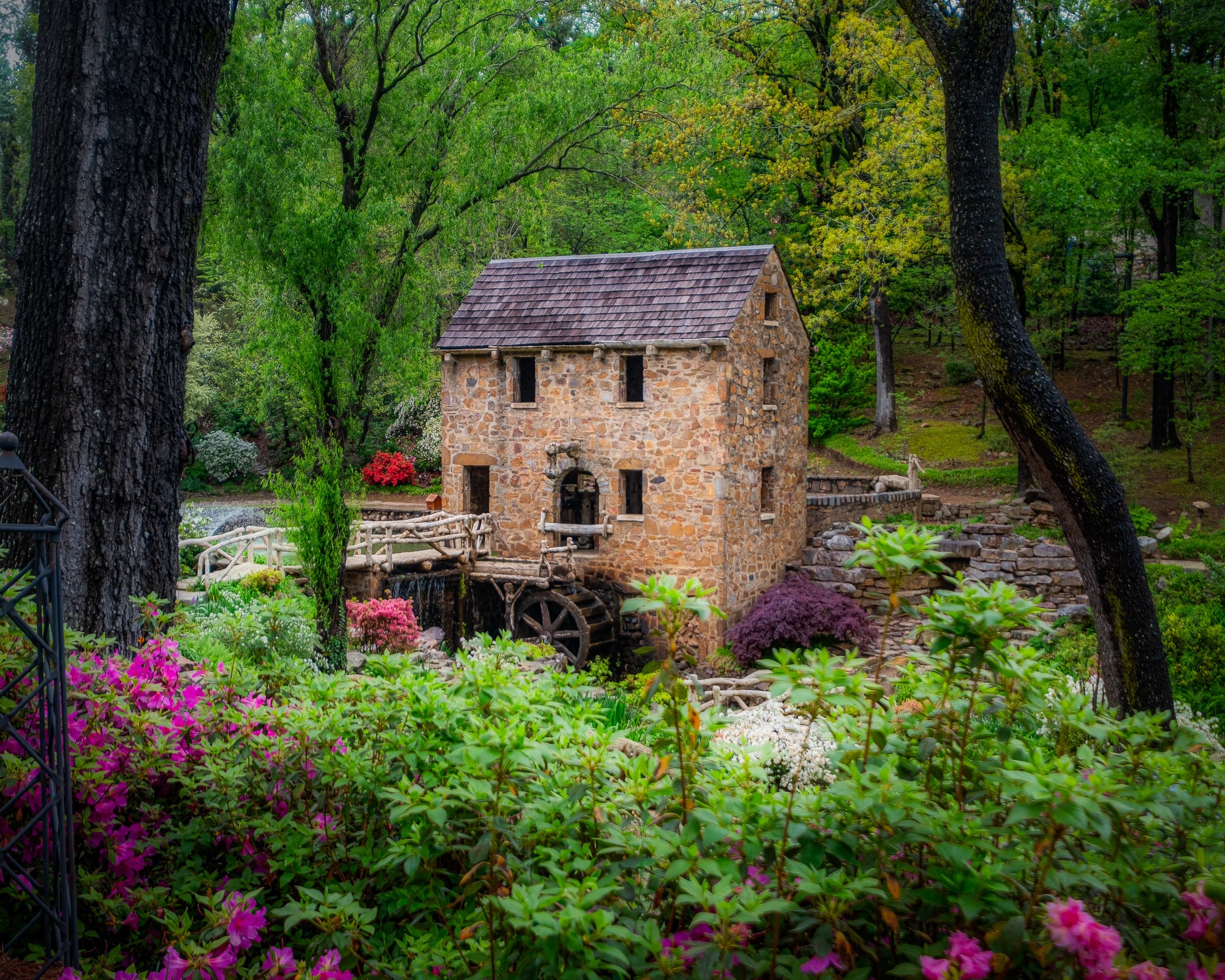 A water mill nestled in trees and flowers