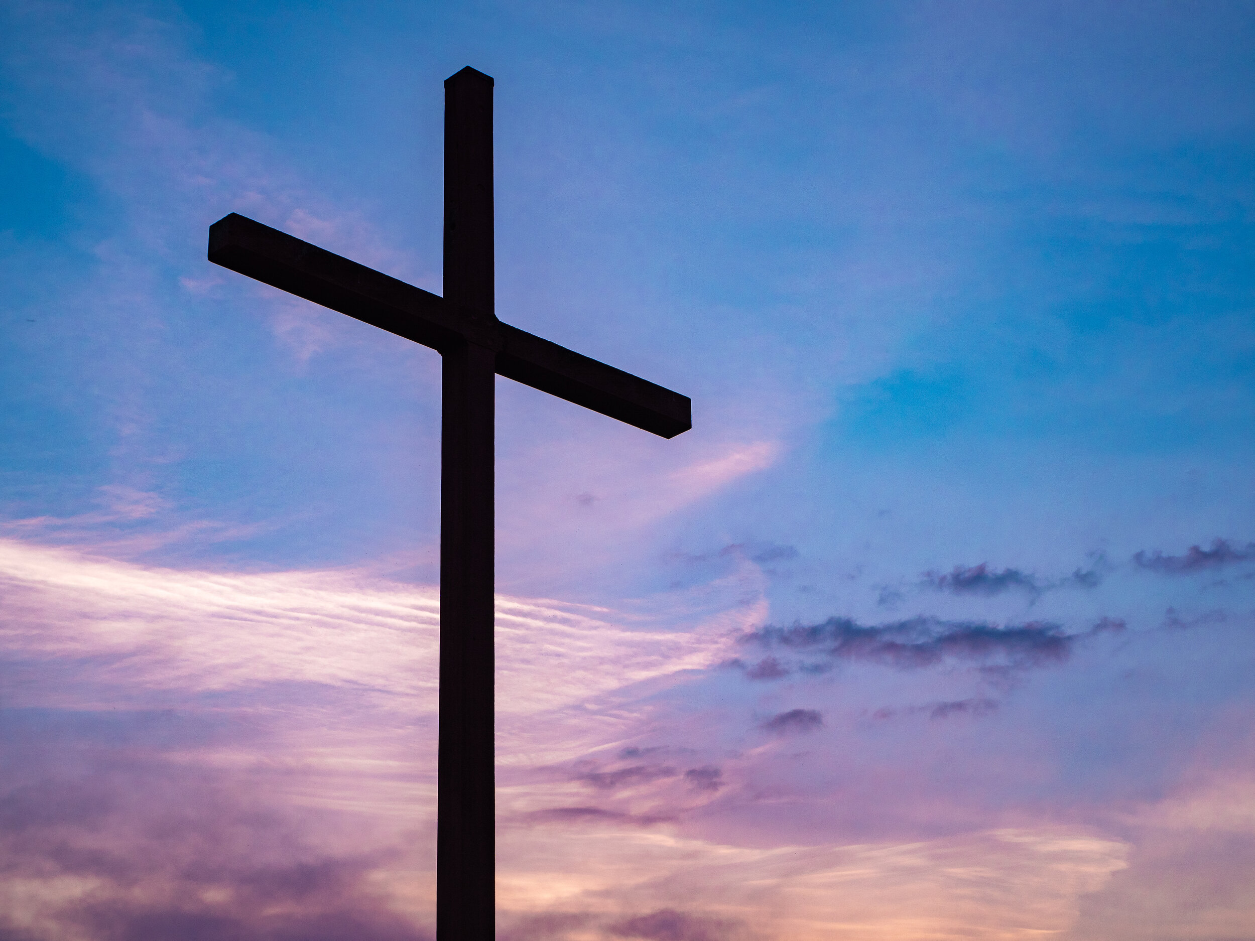 Alt 文本:一個傾斜的木十字架,在由藍色和紫色色調的日出上捕獲。