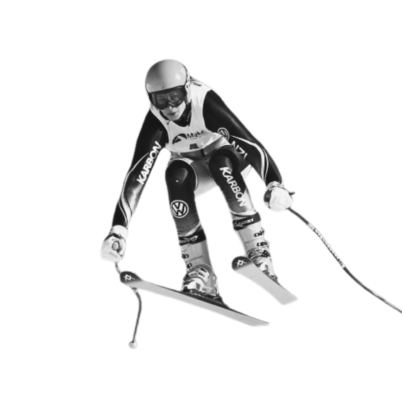 A skier in mid-air during a downhill ski race, wearing a helmet and ski racing gear, holding ski poles, with skis angled downward.