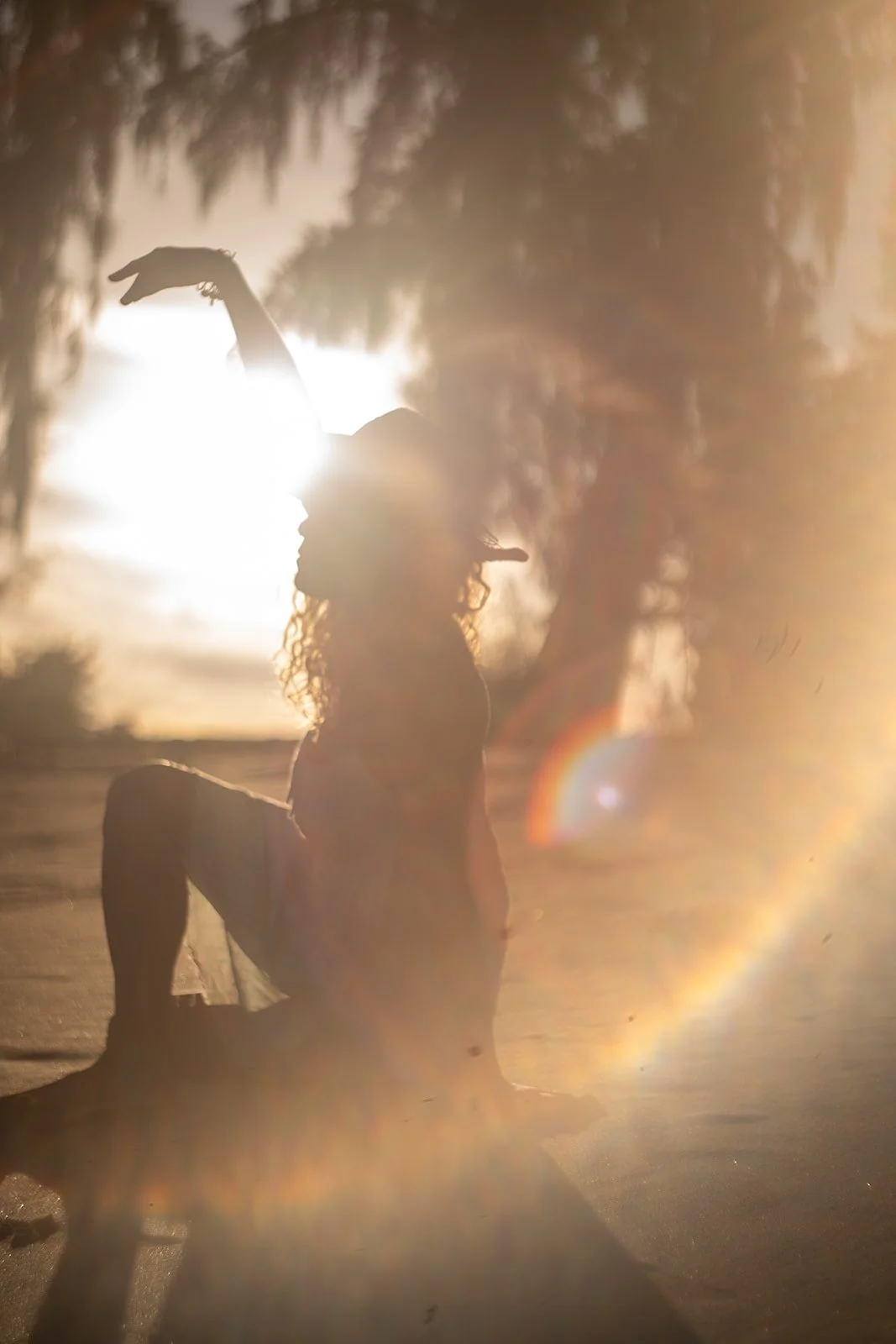 A woman with curly hair sitting outdoors during sunset, with sunlight causing a lens flare in the photo.