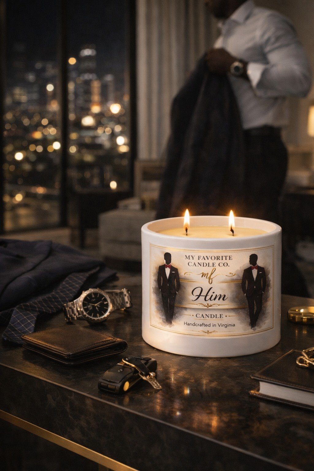 A lit candle labeled 'My Favorite Candle Co. mf Him, Handcrafted in Virginia' with a visible silhouette of a man in a tuxedo on the front, placed on a table alongside a watch, a wallet, keys, and other small items. In the background, a man in a light-colored shirt holds a jacket, with a city skyline visible through a window.