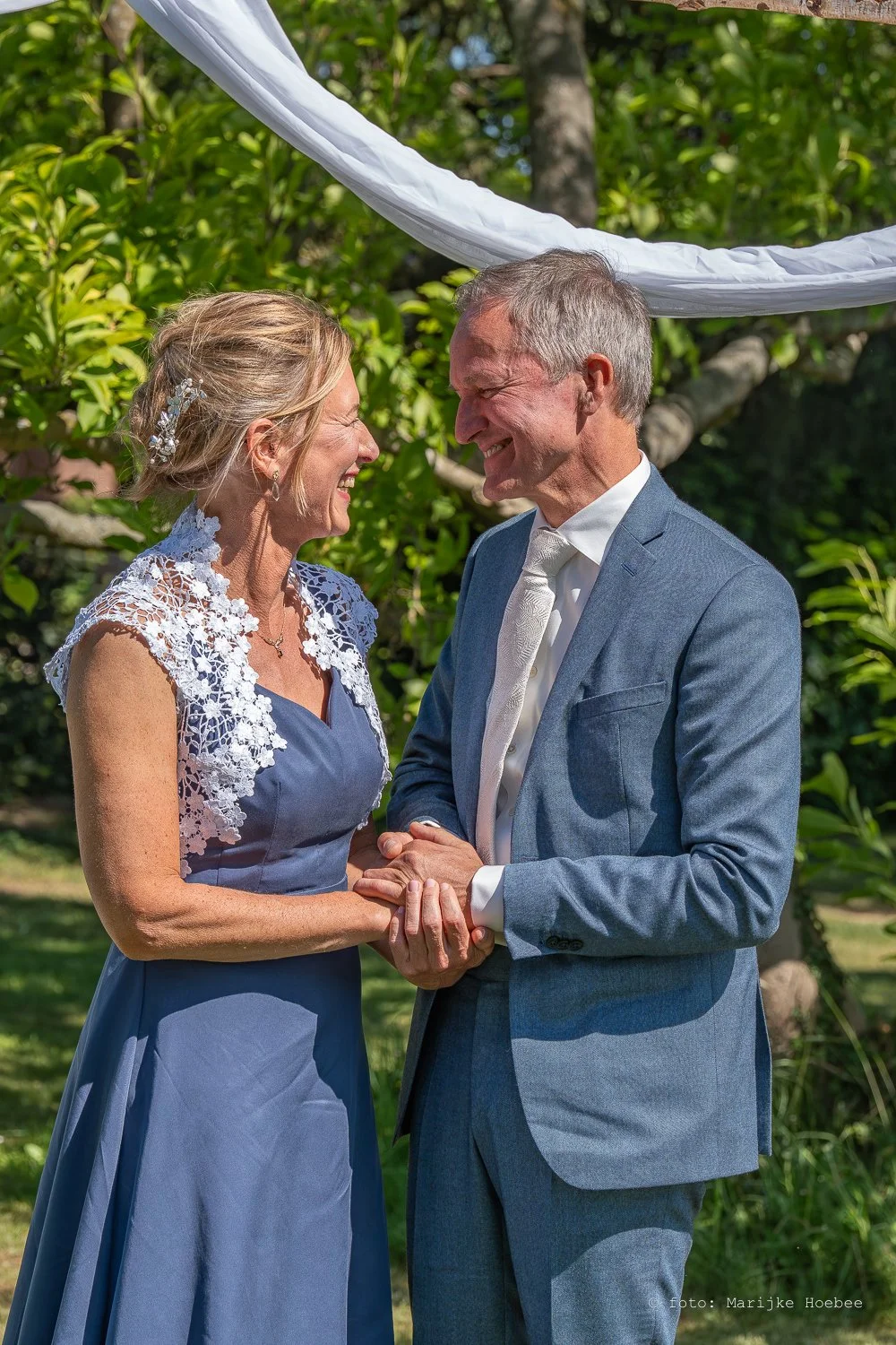 Een stel dat op hun bruiloft in een tuin staat, lachend en hand in hand.