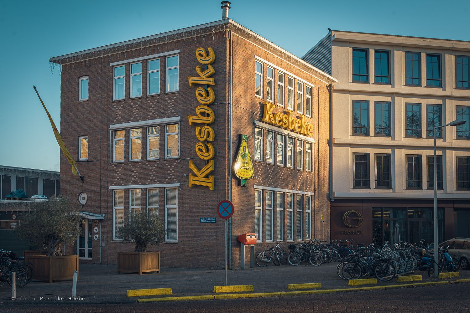 Een gebouw met een grote gele bedrijfsnaam 'Kestecke' en een ander woord 'Kestecke' erbij, met veel fietsen voor de ingang en een blauwe lucht erboven.