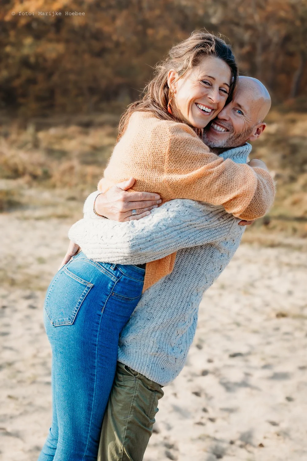 Een paar dat elkaar omhelst op een strand tijdens de herfst, lachend en genietend.
