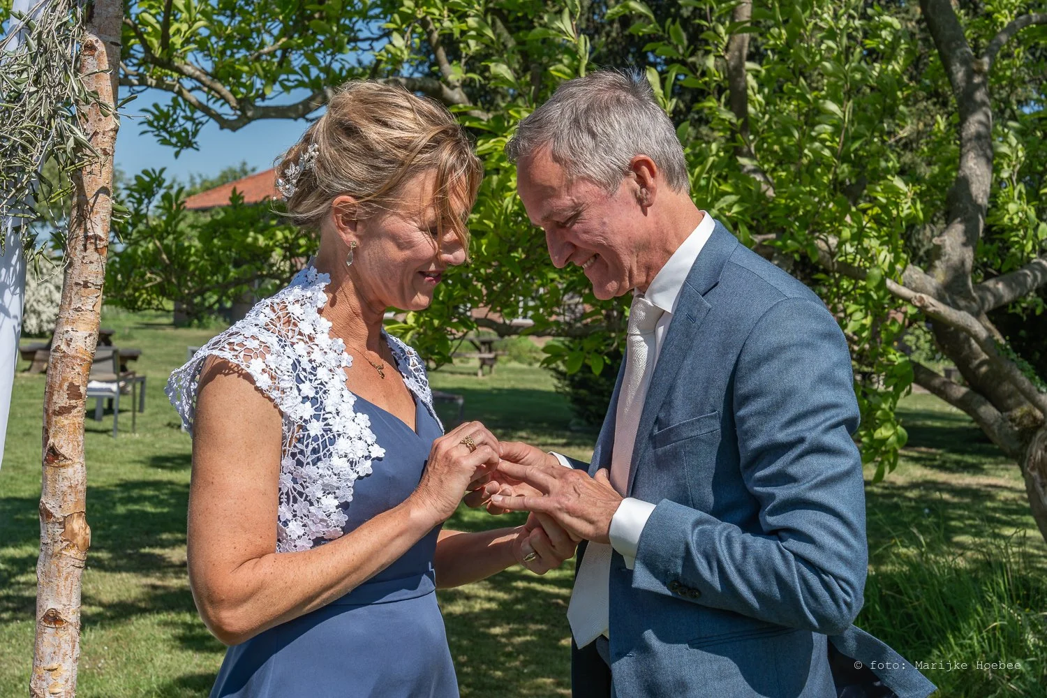 Een getrouwd stel is buiten op een groen grasveld, de vrouw krijgt een ring van de man tijdens een huwelijksceremonie.