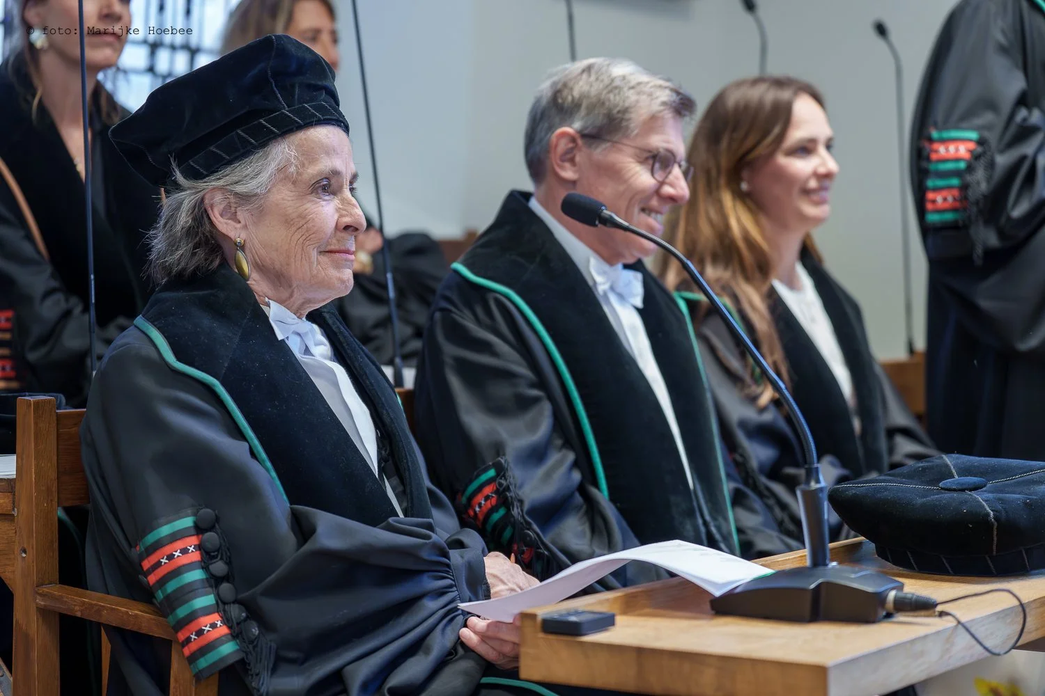 Mensen in formele kleding tijdens een ceremonie in een rechtszaal, met een microfoon op tafel.