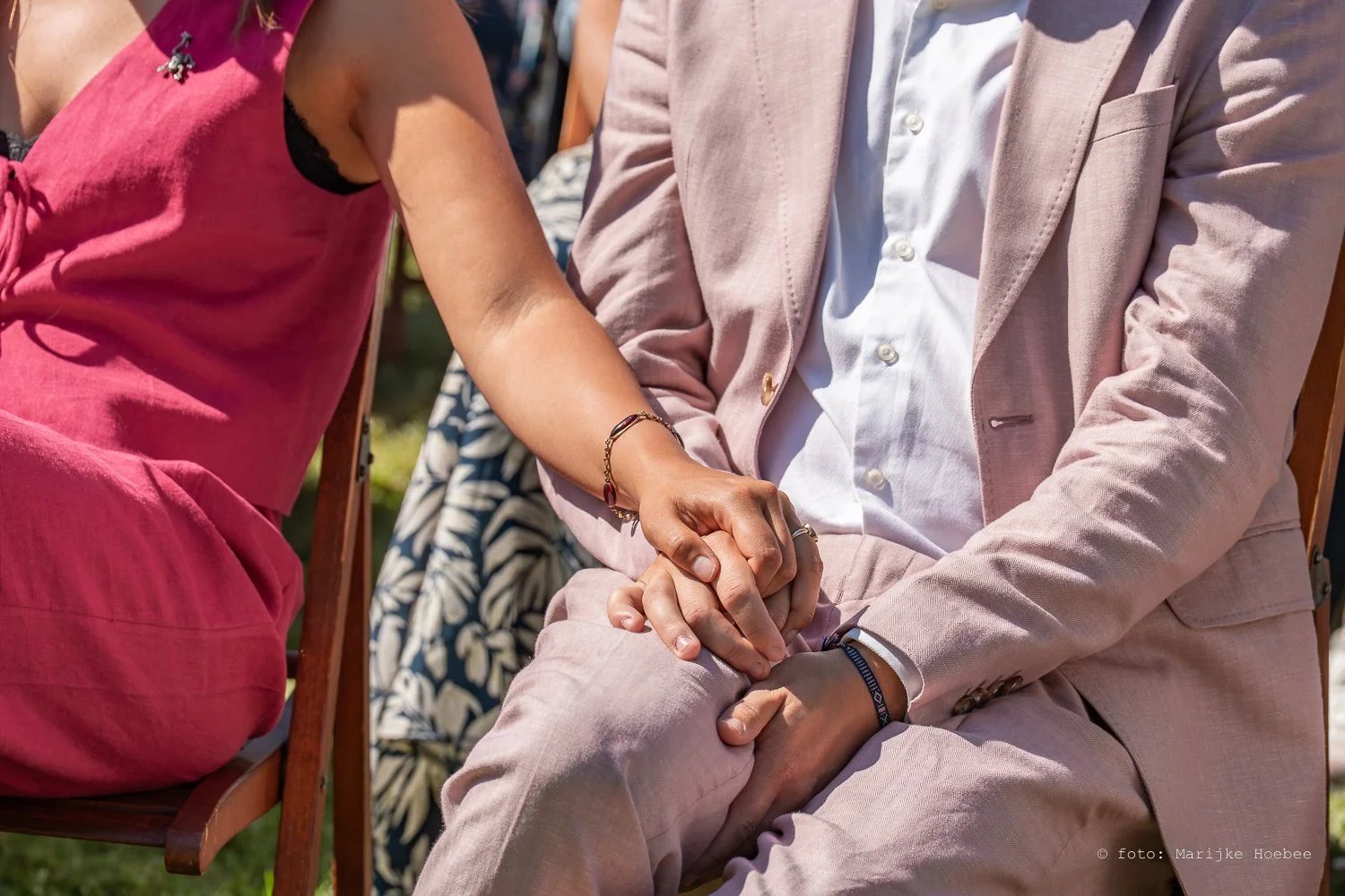 Twee mensen houden elkaars handen vast op hun schoot tijdens een buitenbijeenkomst.