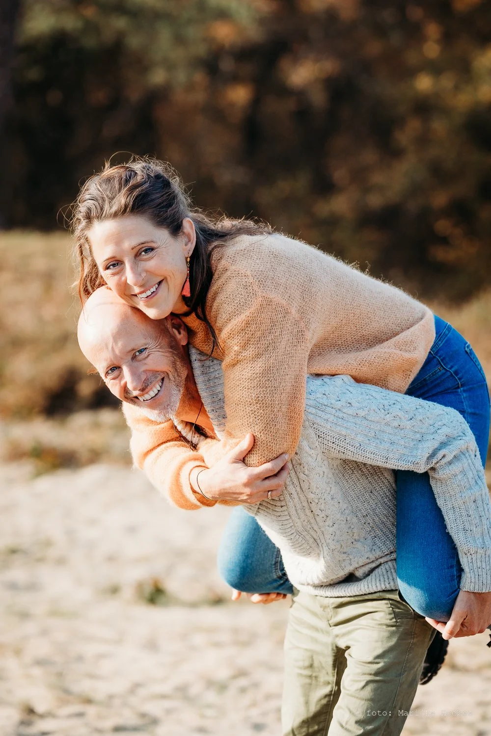 Twee mensen die plezier hebben, de vrouw zit op de schouders van de man, beiden glimlachen, buiten in de natuur.