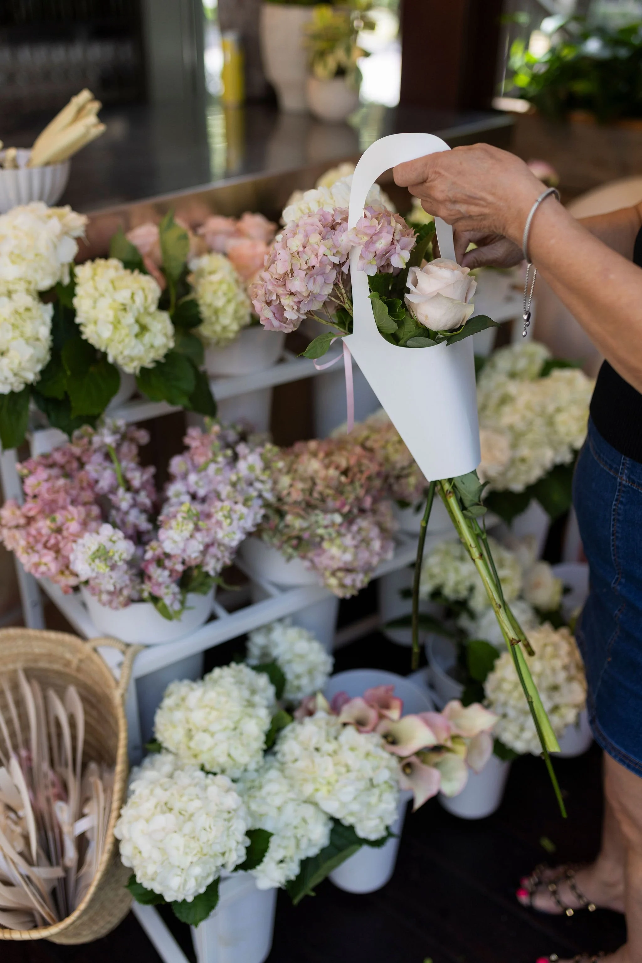 A person arranging light pink and white hydrangea flowers on a table at a flower shop.