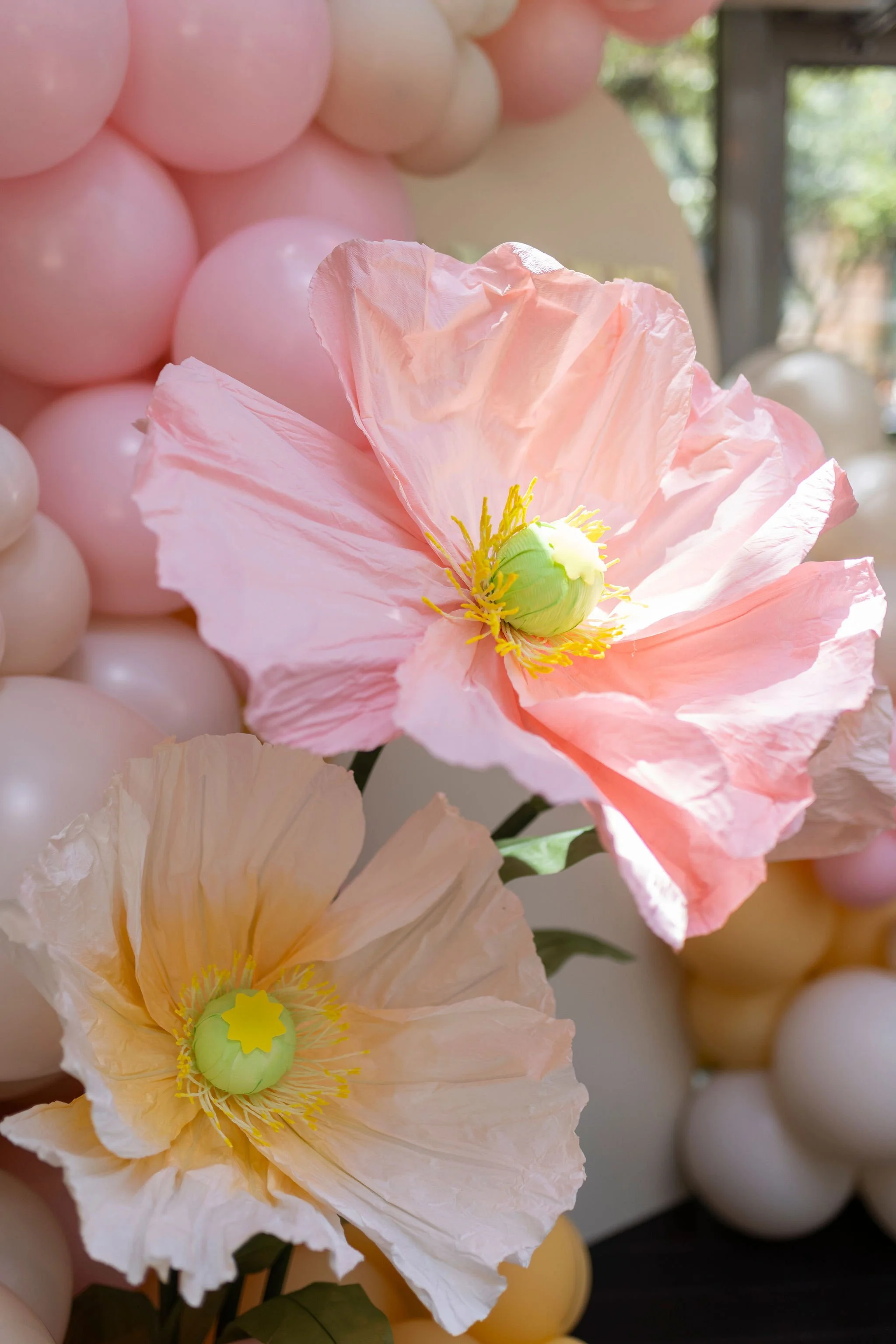 Close-up of pink and cream-colored paper flowers with green centers, part of a decorative balloon arrangement in the background.