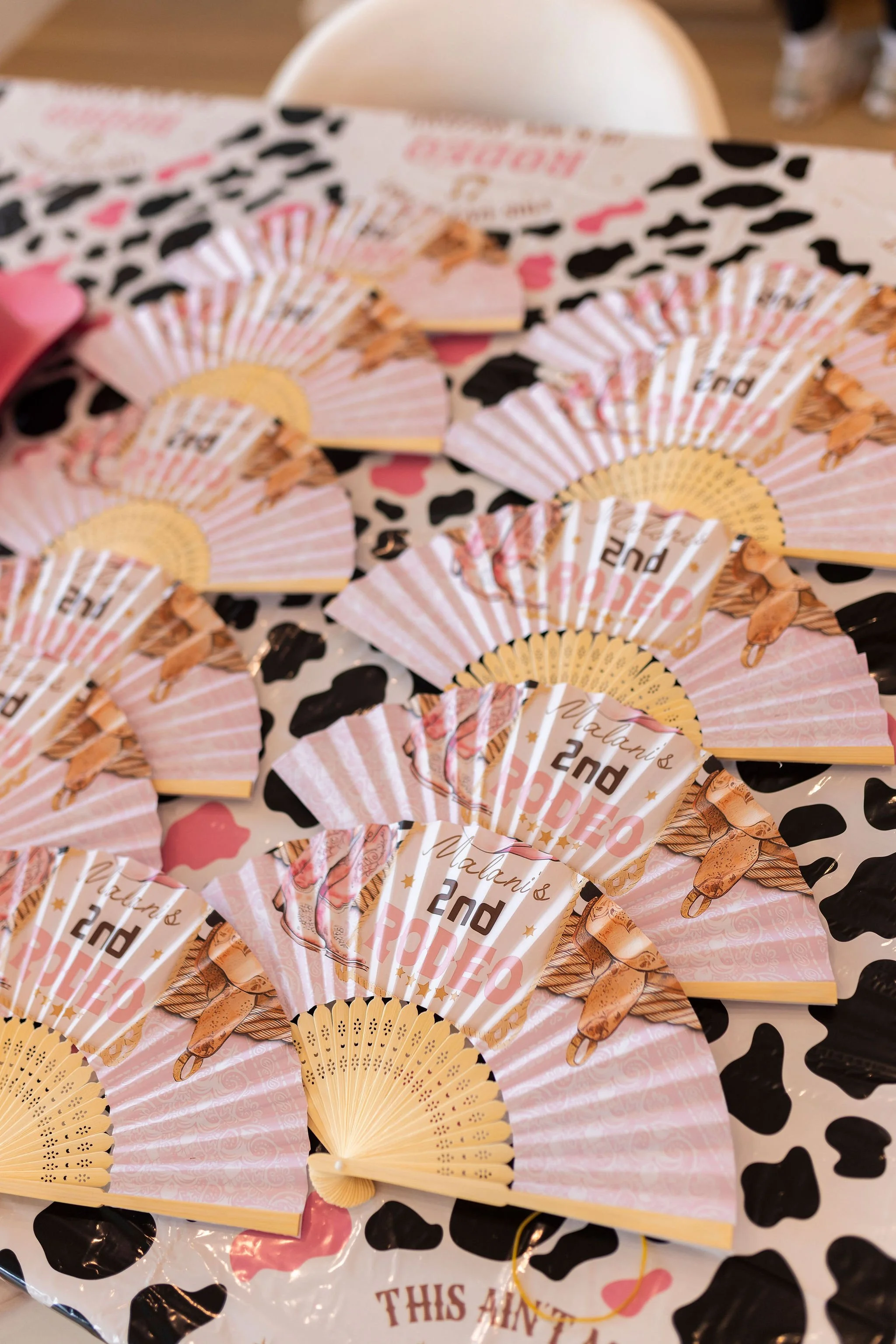 Decorative paper fans with a princess theme and printed text celebrating a second birthday, on a table with a black and white heart-patterned tablecloth.