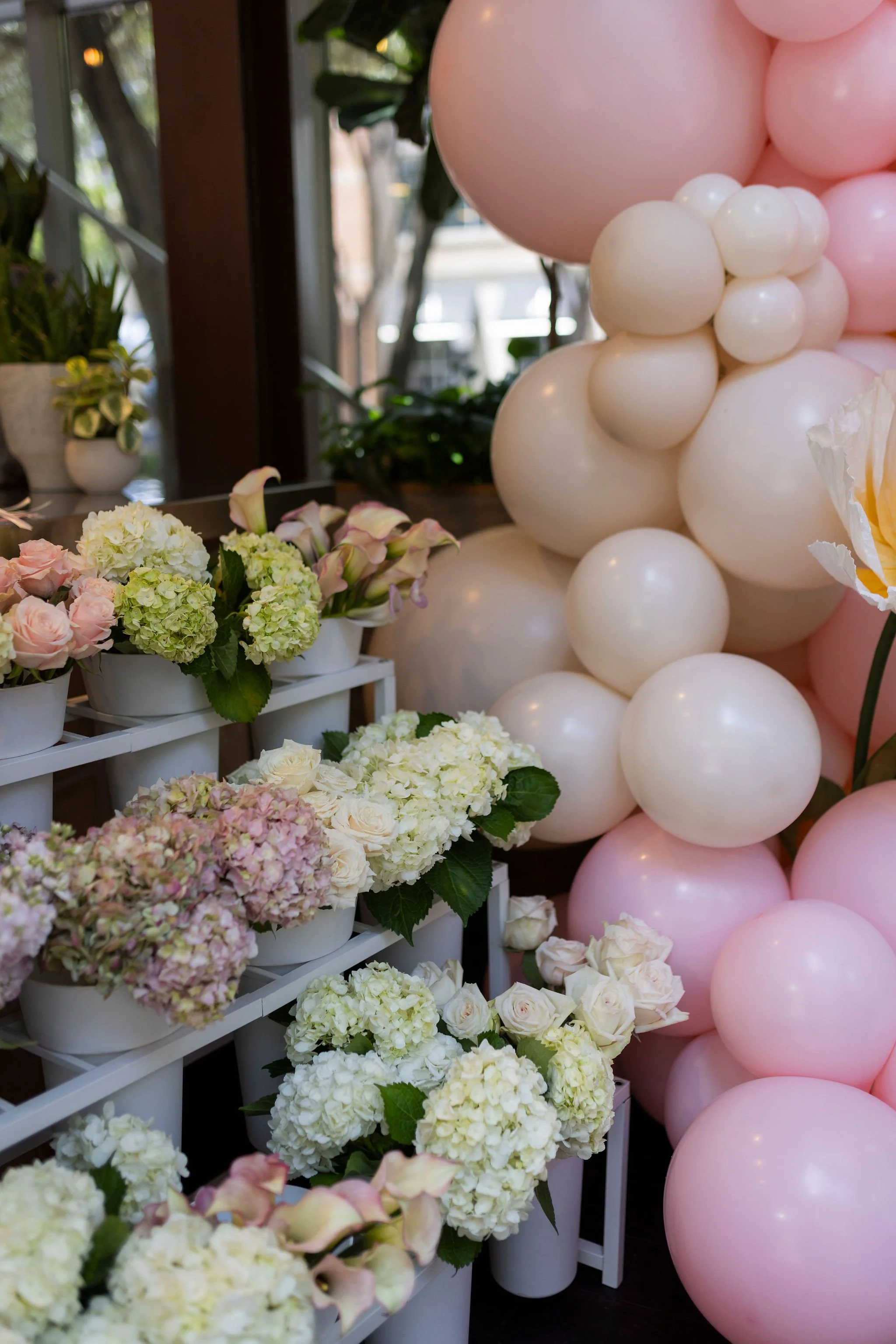 Arrangement of white, pink, and cream flowers next to a cluster of pink and white balloons.