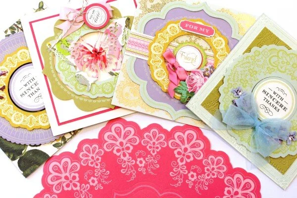 A collection of colorful greeting cards with floral and decorative designs, featuring ribbons and ornate borders.