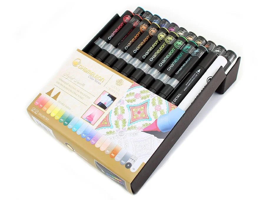 A set of 22 Chameleon alcohol markers in various colors arranged in a black and gold box, with some markers displayed on a sheet of paper showing a colorful design and coloring example.