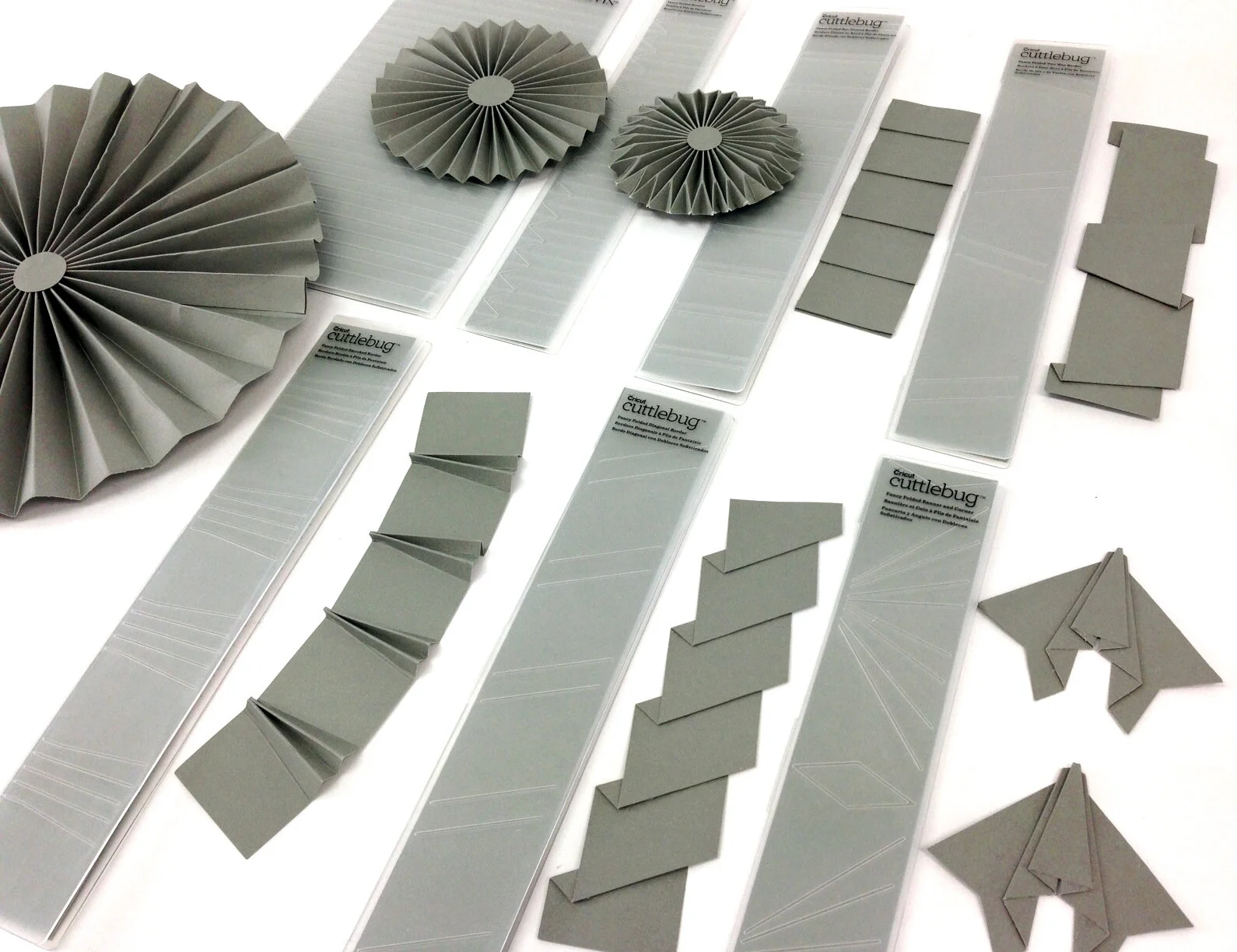Various light gray paper crafting supplies, including paper fans, folded paper pieces, and adhesive sheets, arranged on a white surface.