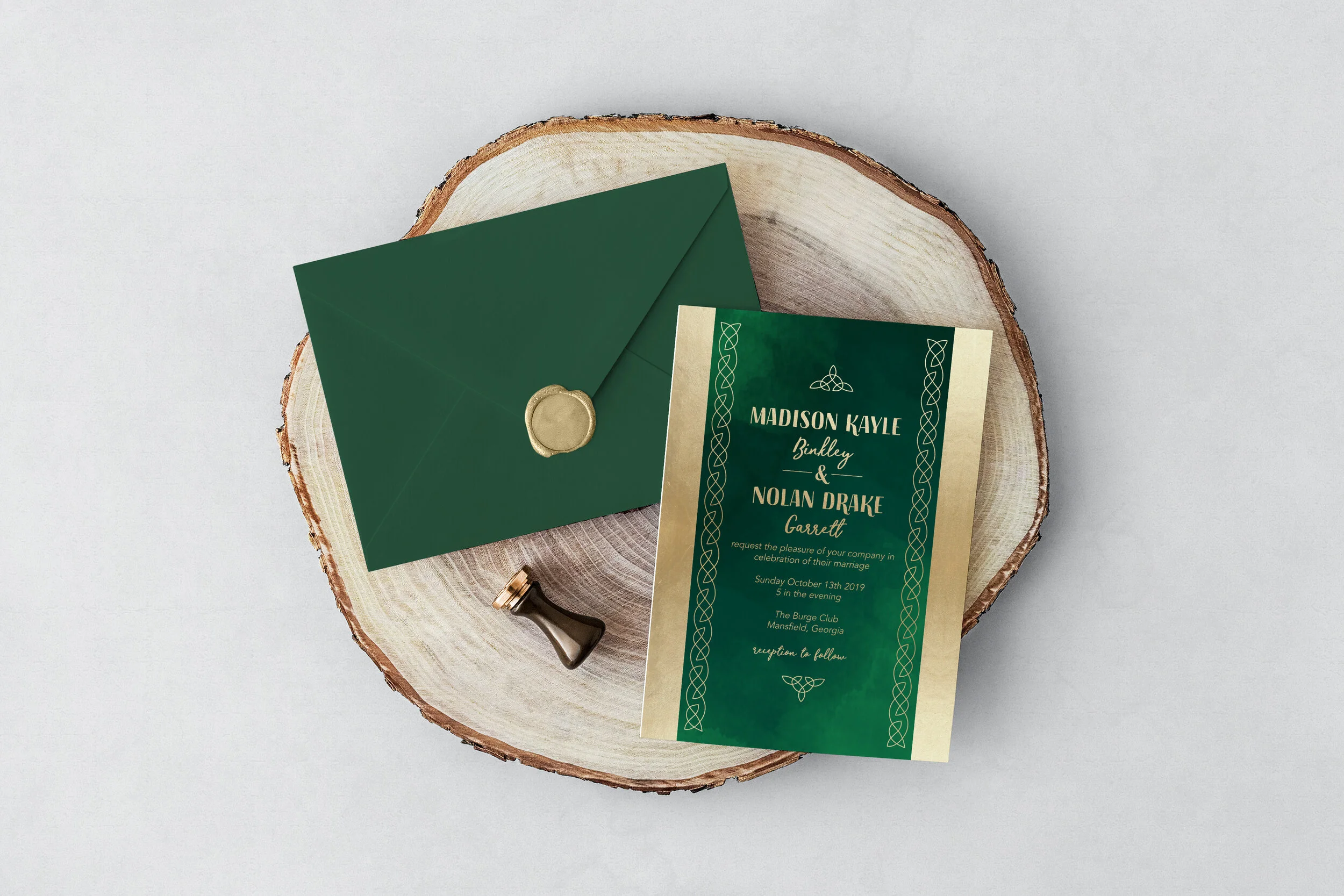 Wedding invitation, green envelope with gold seal, and a detail stamp on a wooden slab.