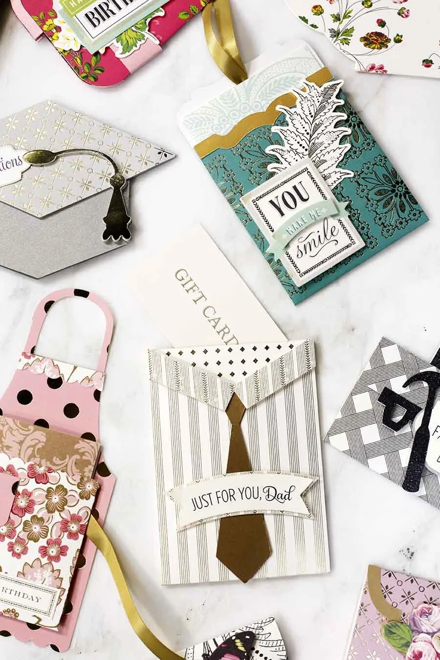 Assorted greeting cards and gift tags, including a card with a tie illustration and the message 'Just for you, Dad,' a gift bag with the message 'You make me smile,' and other floral and patterned cards.