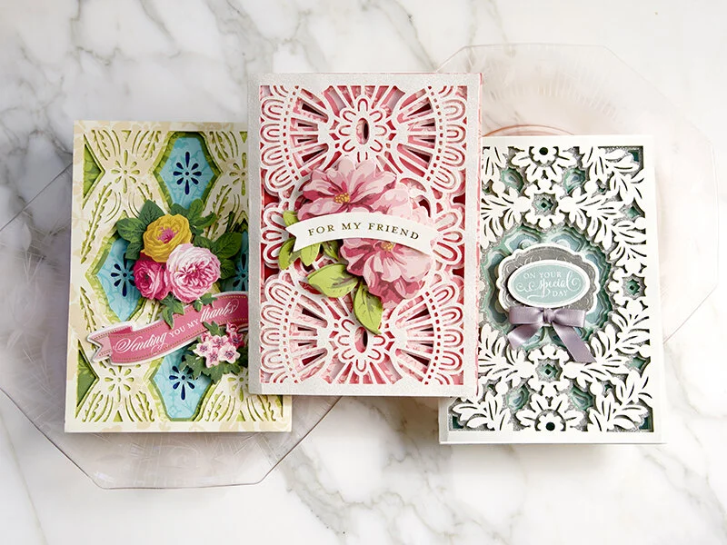 Three decorative greeting cards with floral and intricate cut-out designs, placed on a marble surface.