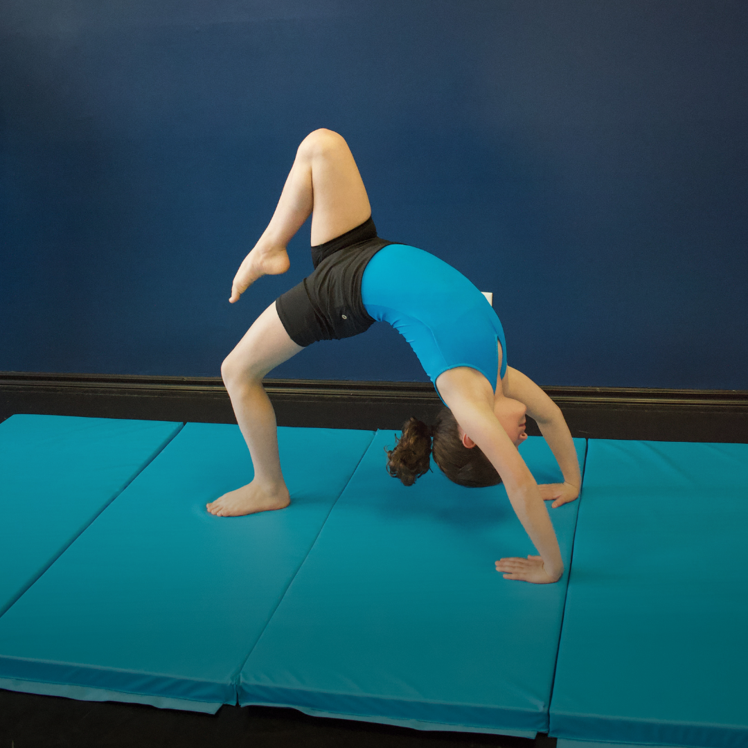 A young girl practicing a yoga pose on a blue mat indoors.