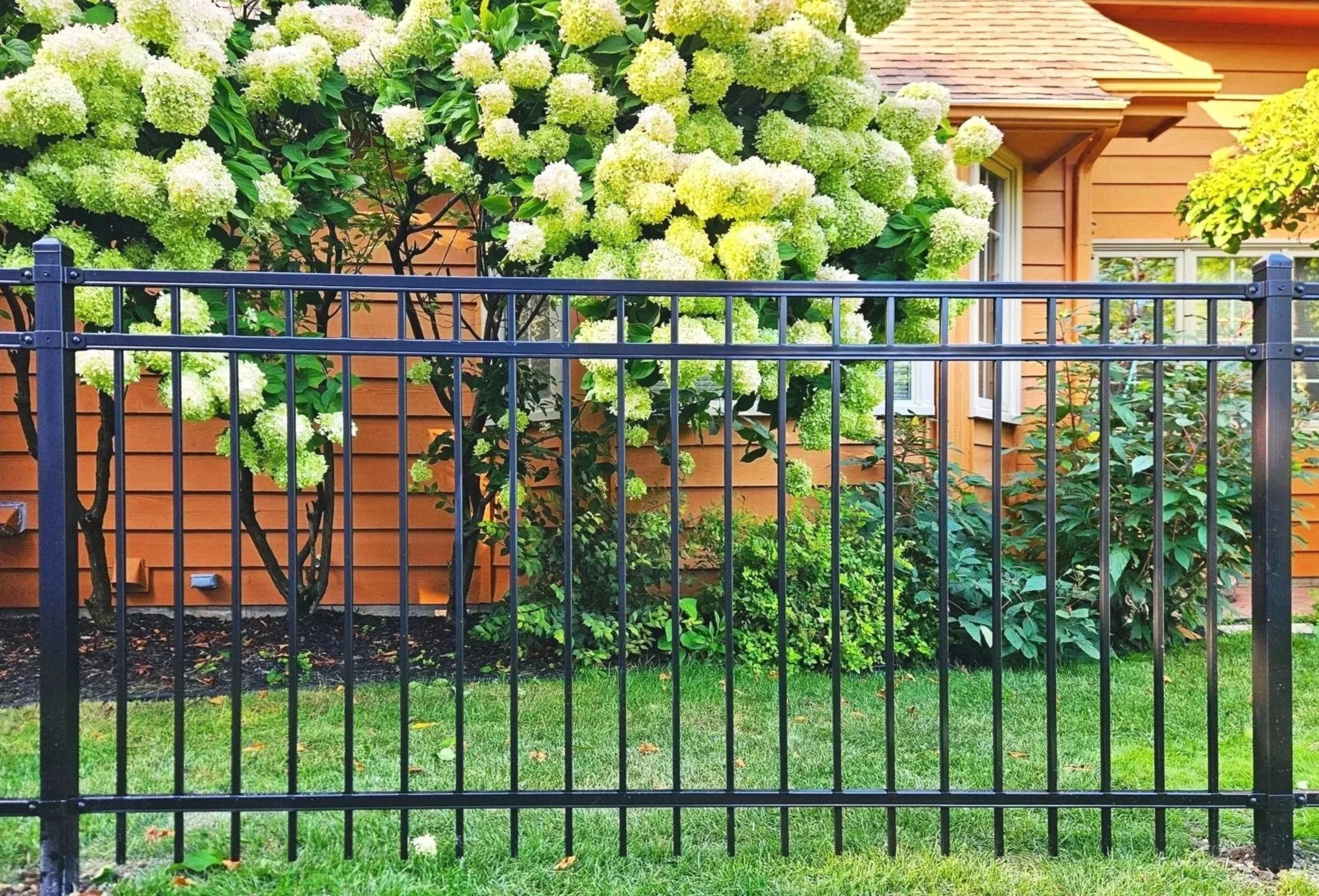 Outdoor playground with artificial green turf, surrounded by a black metal fence.