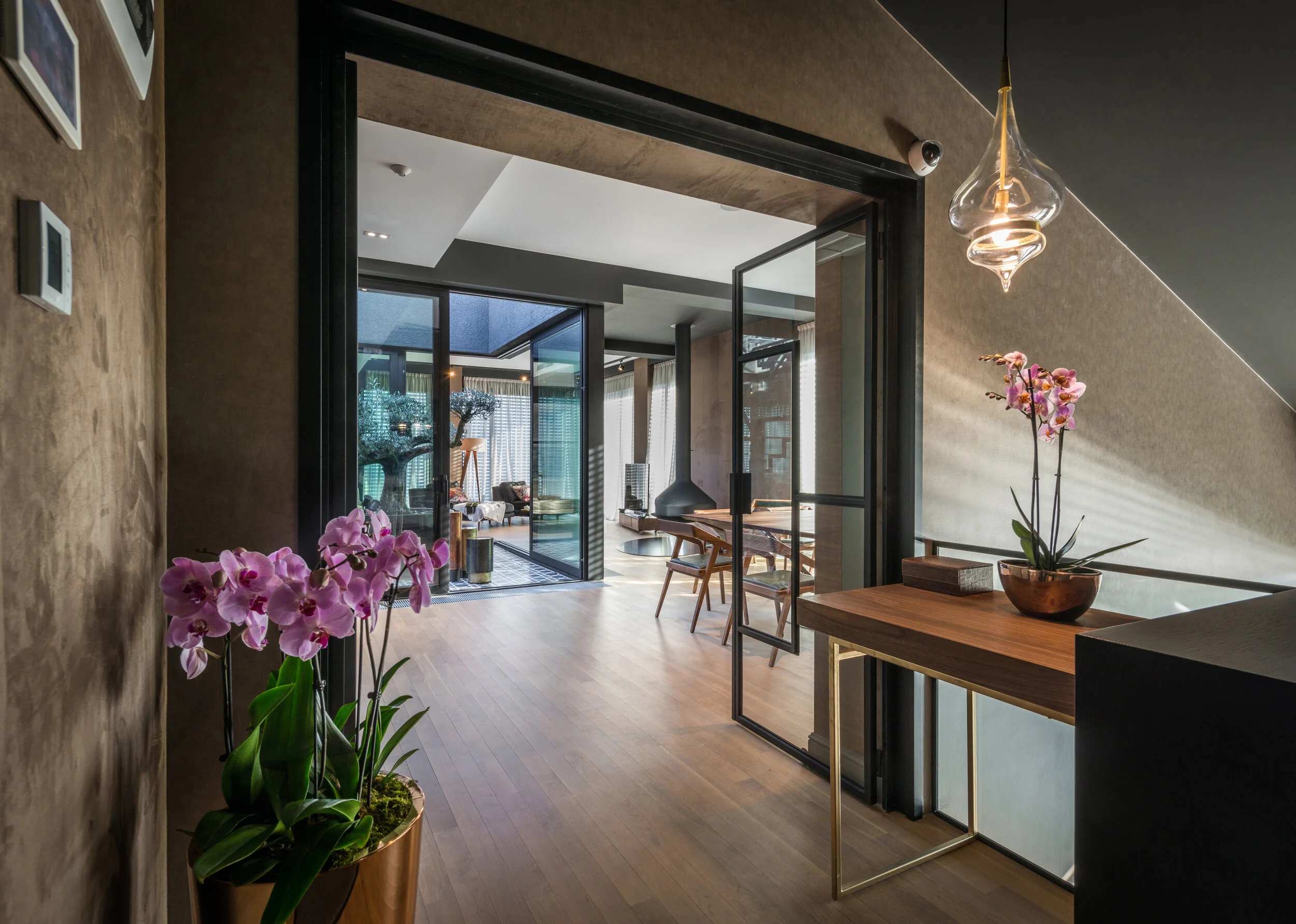 Modern interior living space with wood flooring, glass doors, a dining area, and pink orchids in a copper pot.