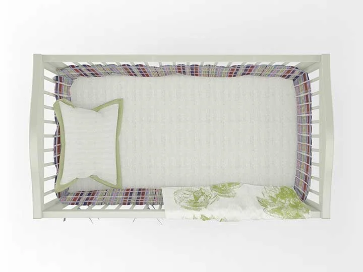 White crib with colorful plaid woven bumper, matching white pillow with green trim, white fitted sheet, and green patterned blanket inside the crib.
