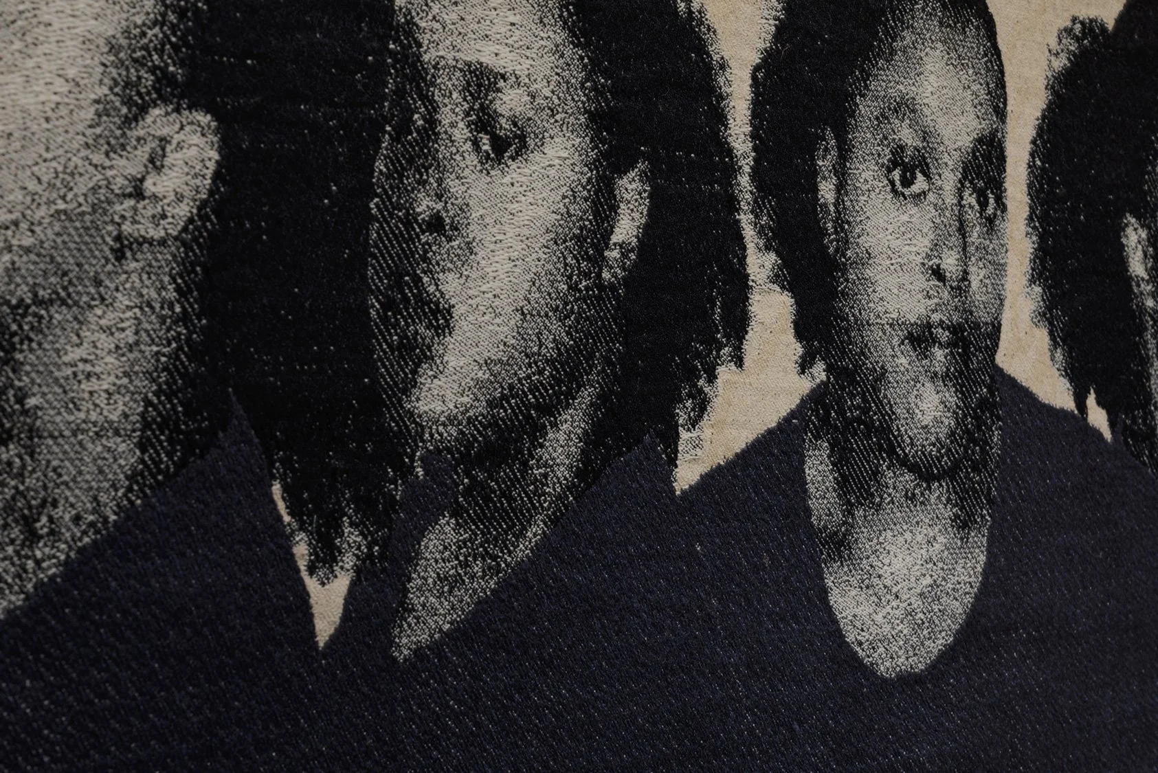 Close-up of woven horizontal tapestry installation.  Of the four faces featured, two are in view, looking in different directions with different emotions.