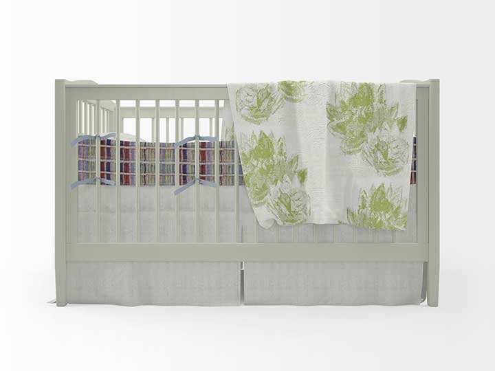 A white crib with a quilted blanket draped over one side, and a colorful striped blanket inside, set against a plain white background.