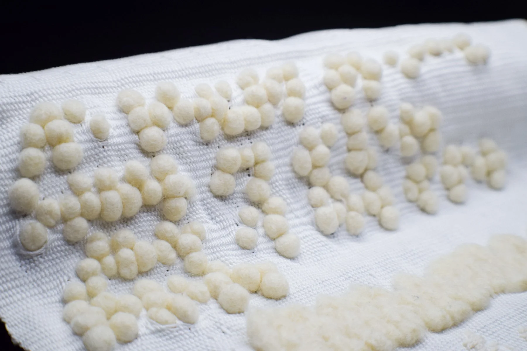 Close-up of white round felt braille balls woven into a woven white ground.