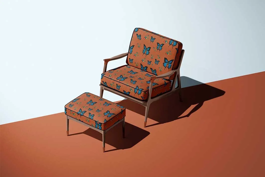 A chair with orange upholstery decorated with blue butterflies, accompanied by a matching ottoman, against a plain background with shadows.