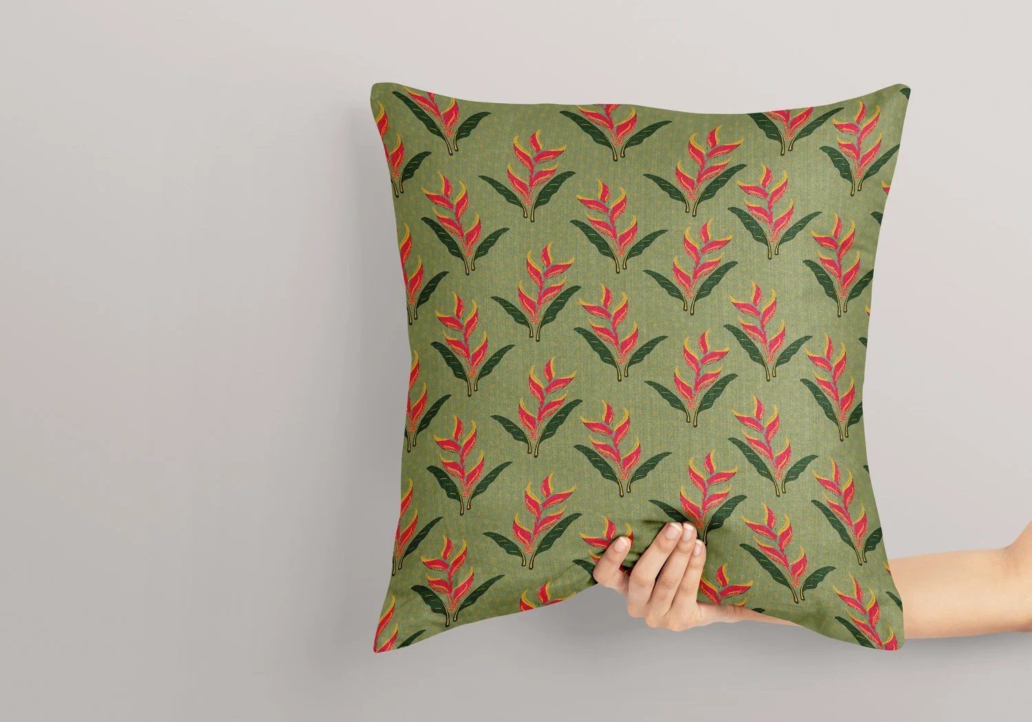 Person holding a green pillow with red and pink floral pattern against a plain background.