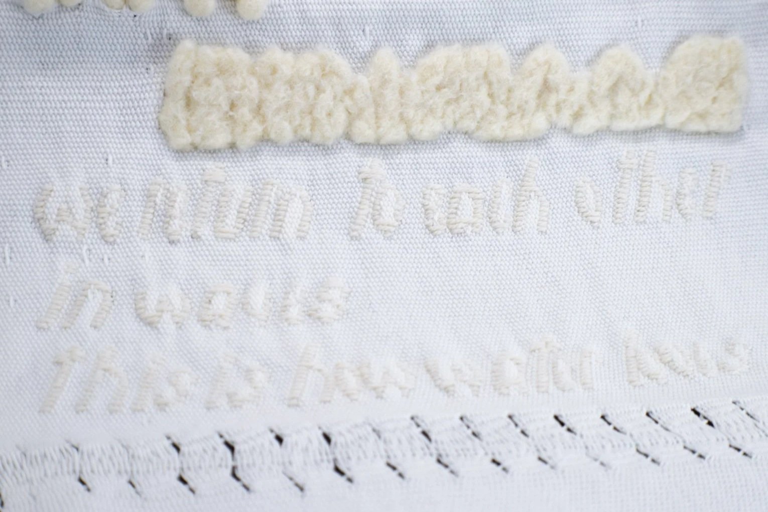 Close-up of woven white fabric with a textured off-white felted wave and faint white text beneath it.