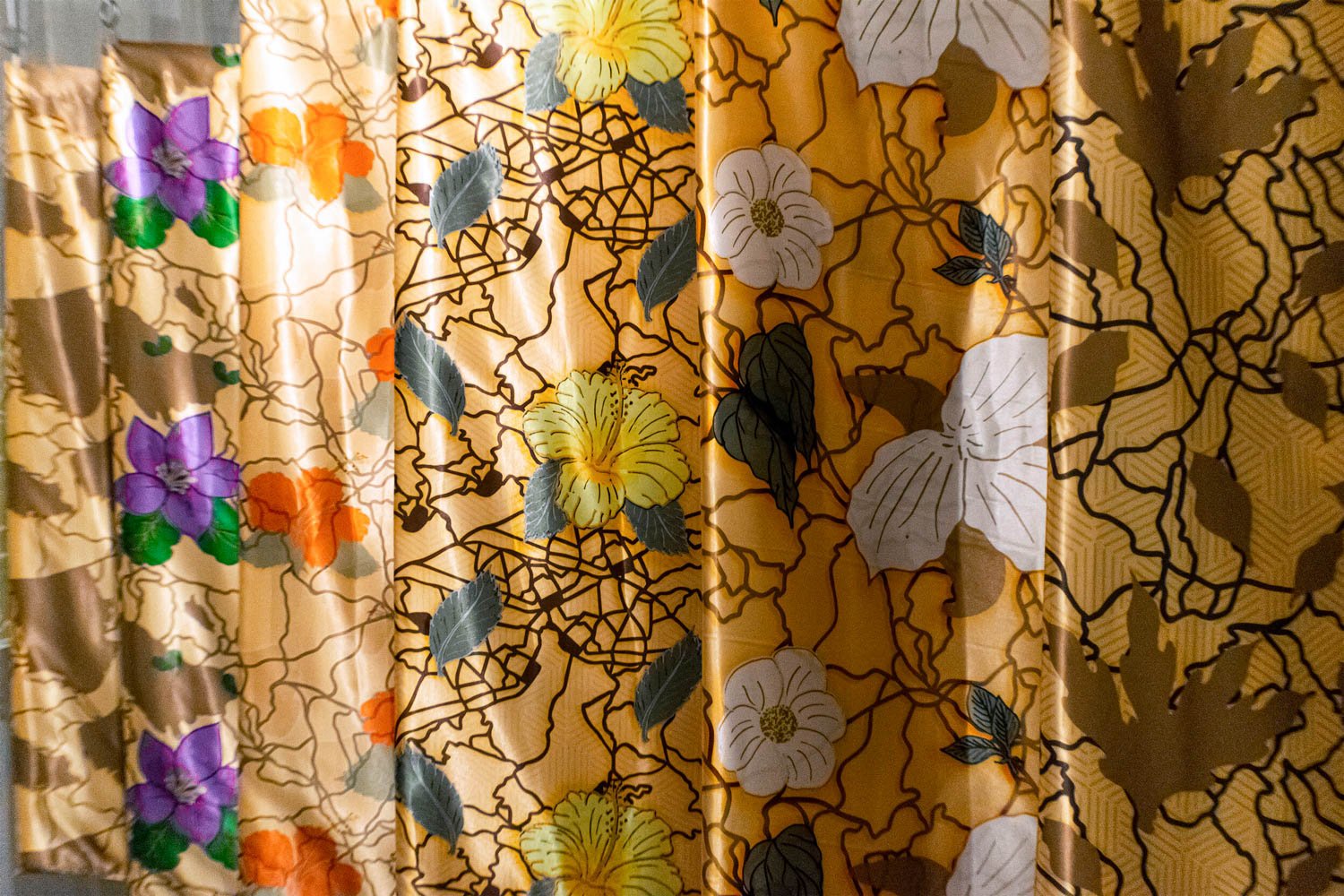 Close-up of floral patterned digitally printed hangings with yellow, purple, orange, and white flowers and green and black leaves.