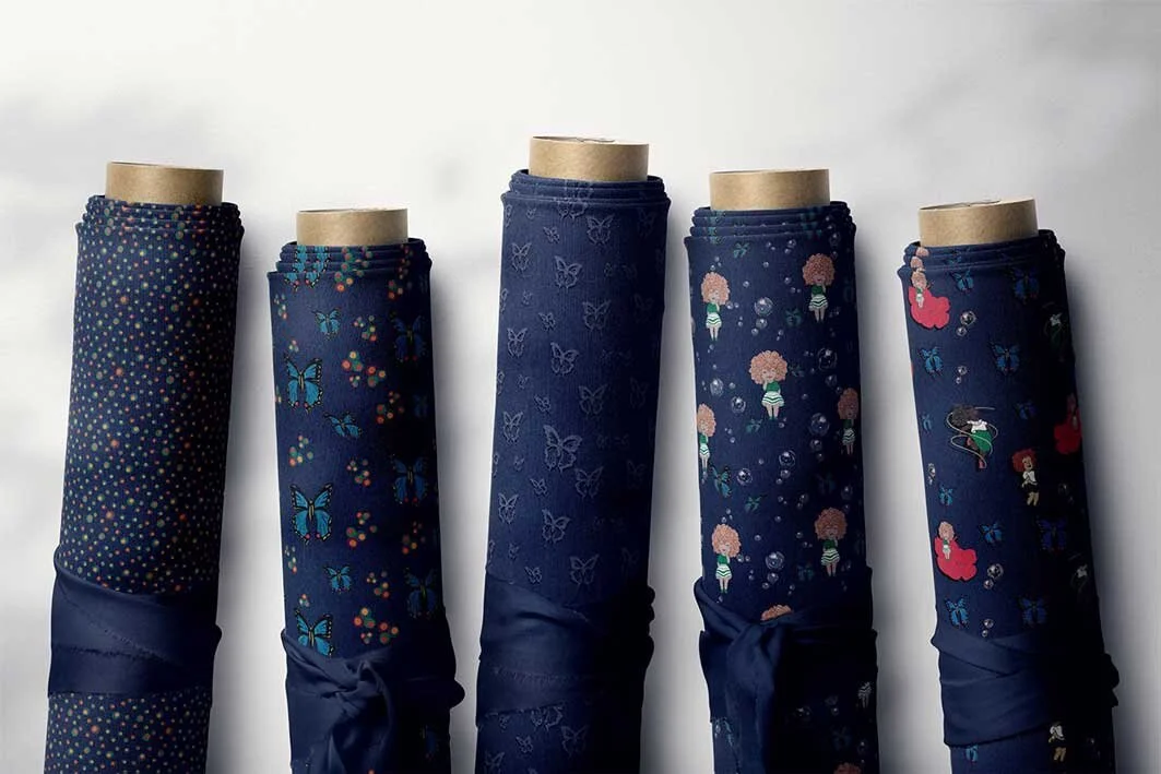 Five fabric rolls with navy blue patterns featuring dots, butterflies, pineapples, flowers, and cartoon characters on a light background.