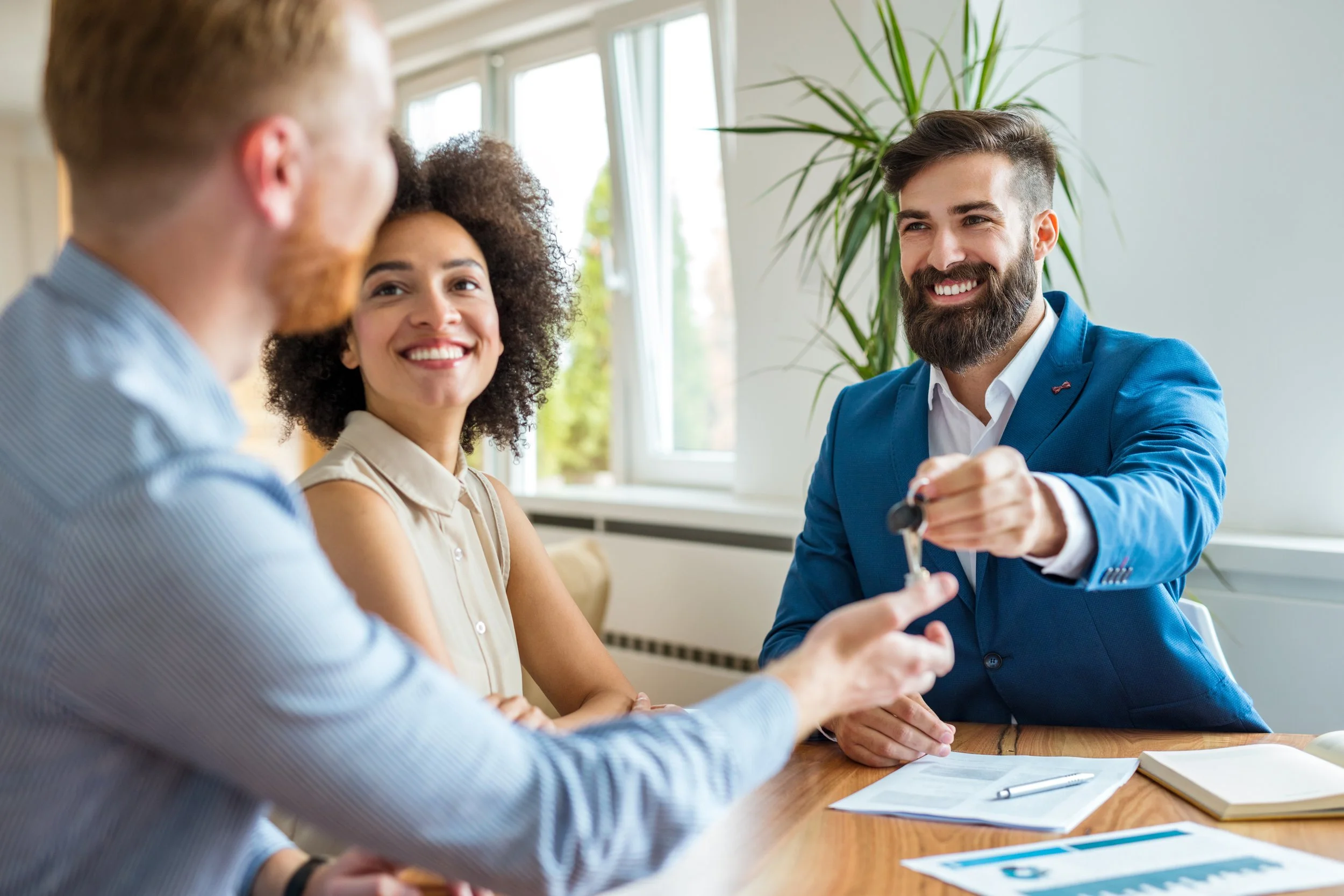 Un homme en costume bleu remet les clés d'une voiture à un autre homme lors d'une rencontre professionnelle, avec deux autres personnes qui sourient dans un bureau lumineux.