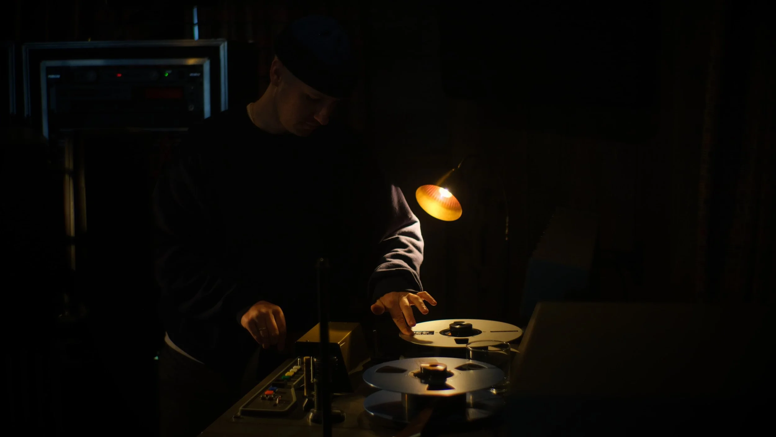 A person working with tape reels in a dimly lit room, illuminated by a small, warm light.