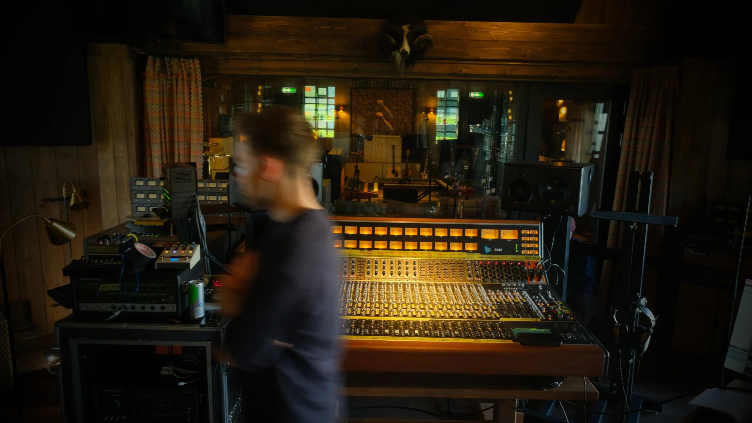Recording studio with a mixing console, speakers, and audio equipment, and a person blurred in motion in the foreground.