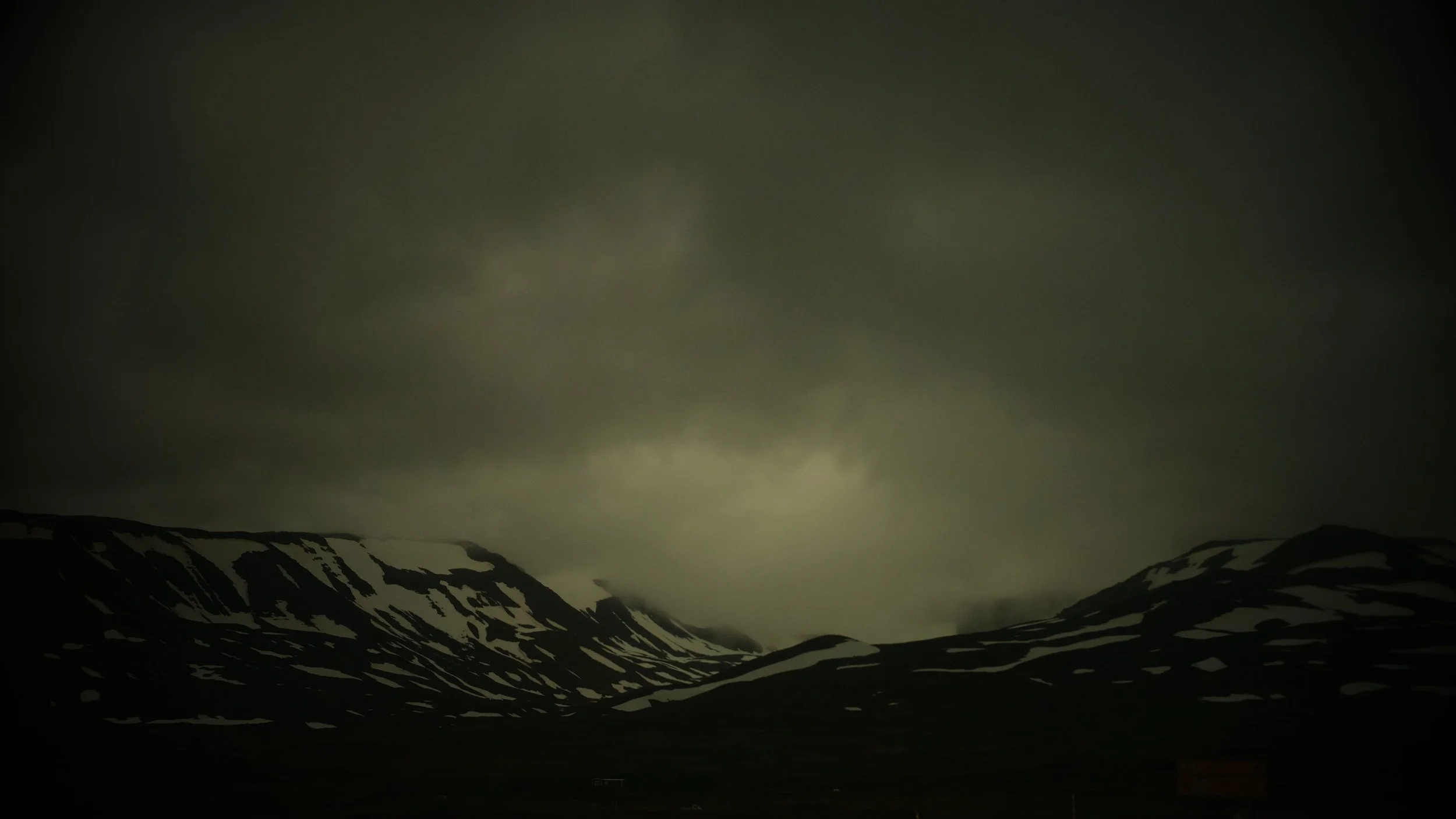 Dark, cloudy sky over snow-capped mountains in a remote landscape