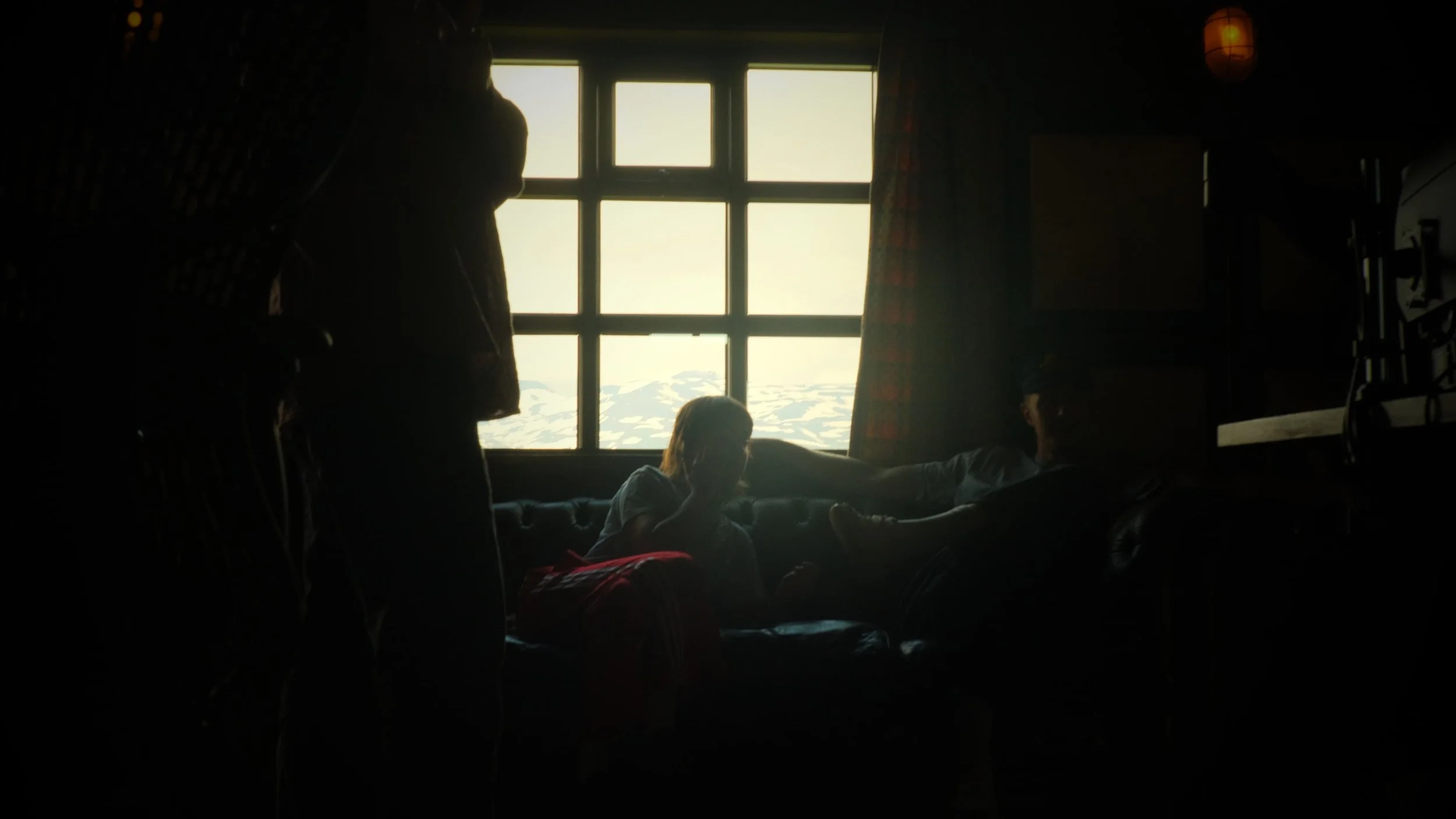 Silhouettes of people inside a dimly lit room with a large window showing snowy landscape outside.