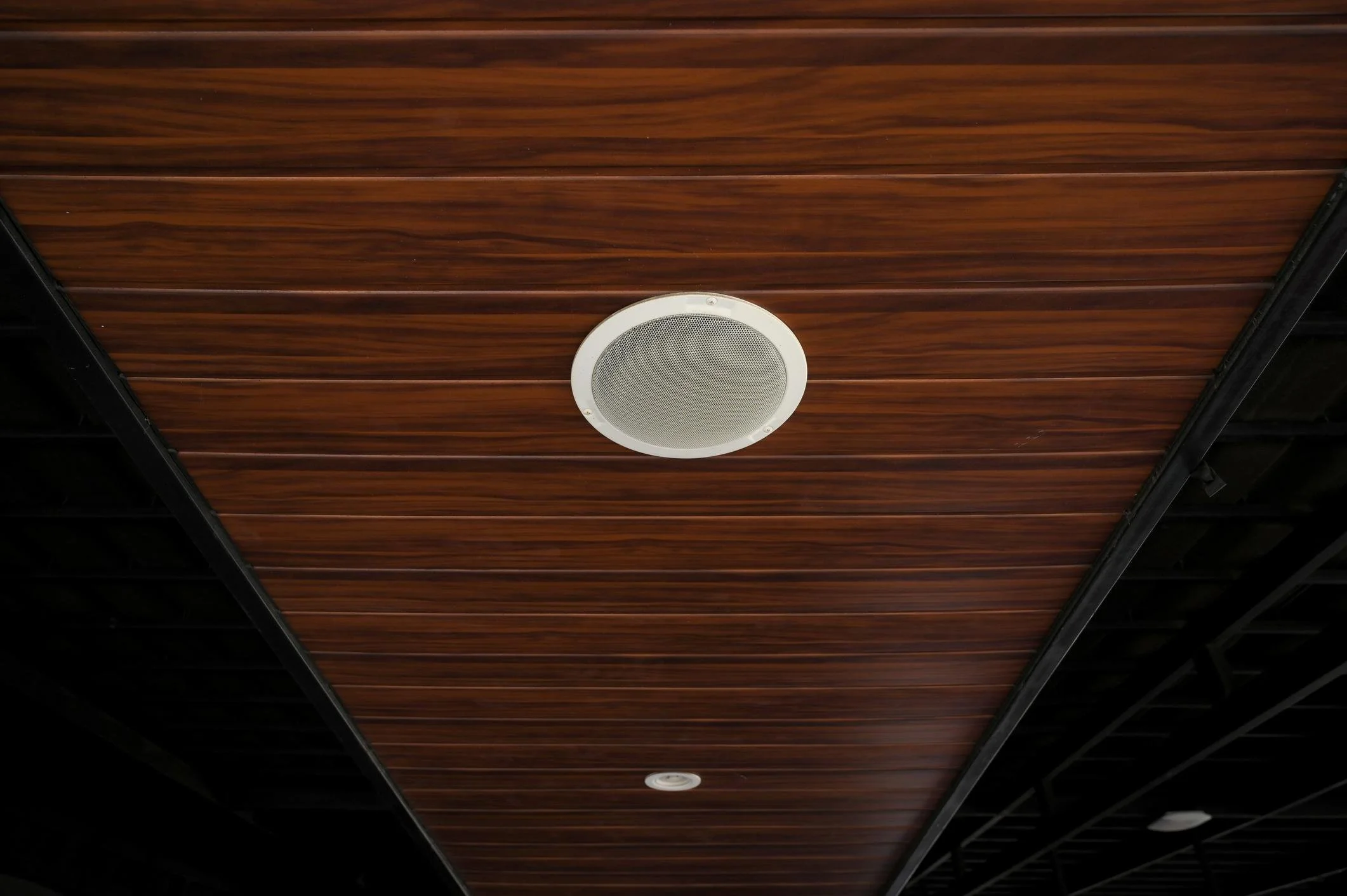 Ceiling with a round speaker and wooden paneling.