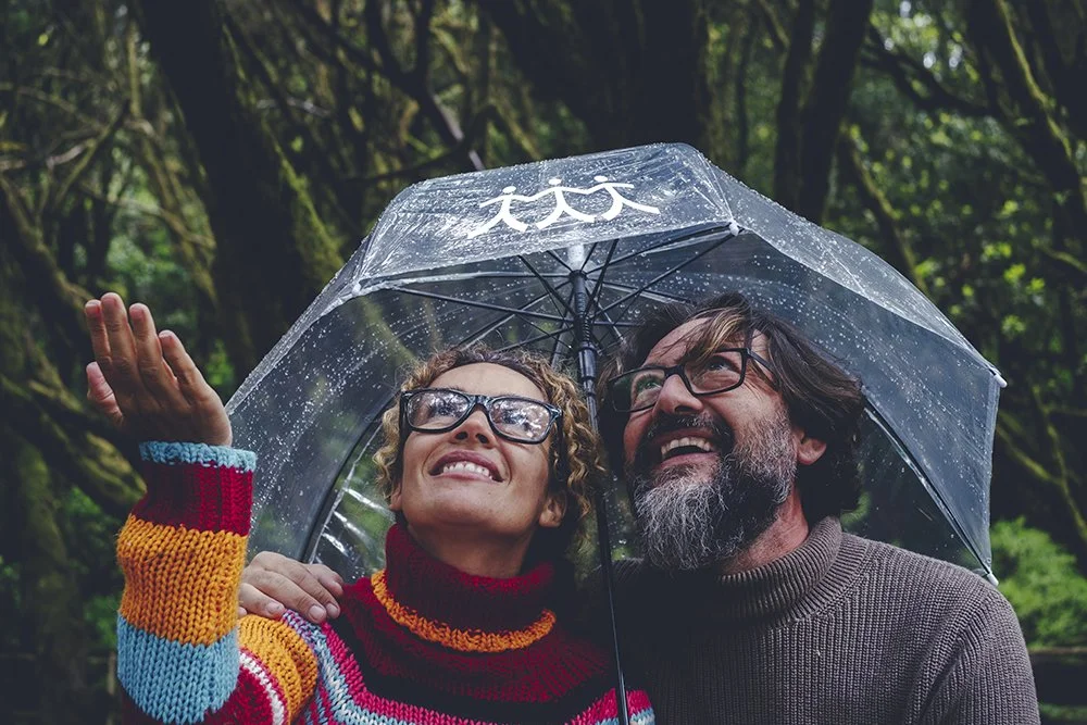 Couple staying dry under an umbrella with the OURCU Peeps icon on it.